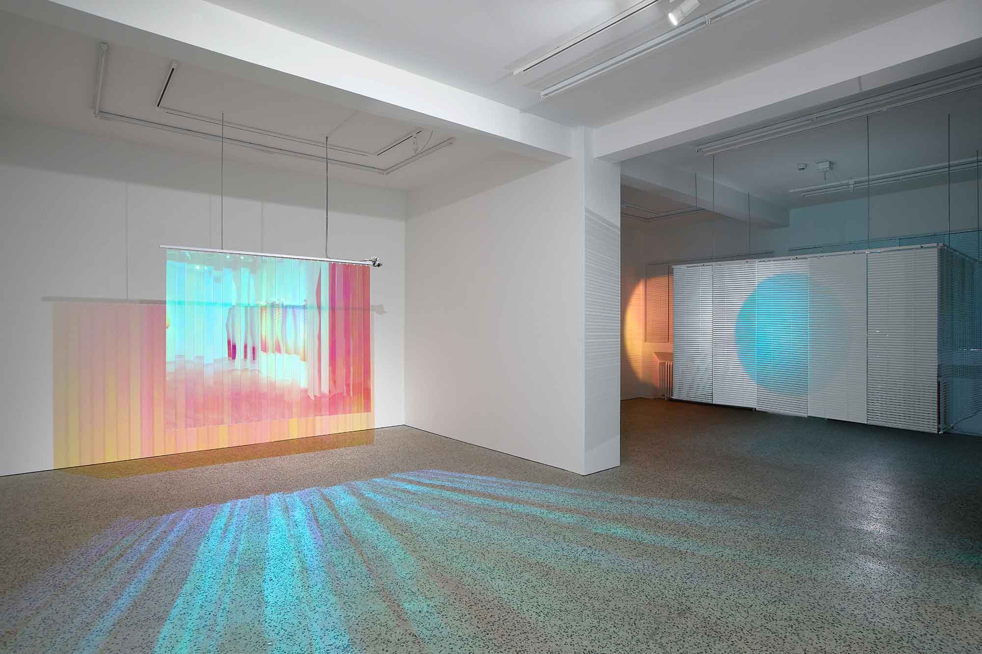 Thordis Erla Zoega, Domestic Sci-fi, installation view: left room showing Everyday hanging dichroic panel with multicolour effect and teal light rays on floor; through glass partition, second room visible with white blind-enclosed structure and blue dichroic circle, BERG Contemporary, Reykjavík