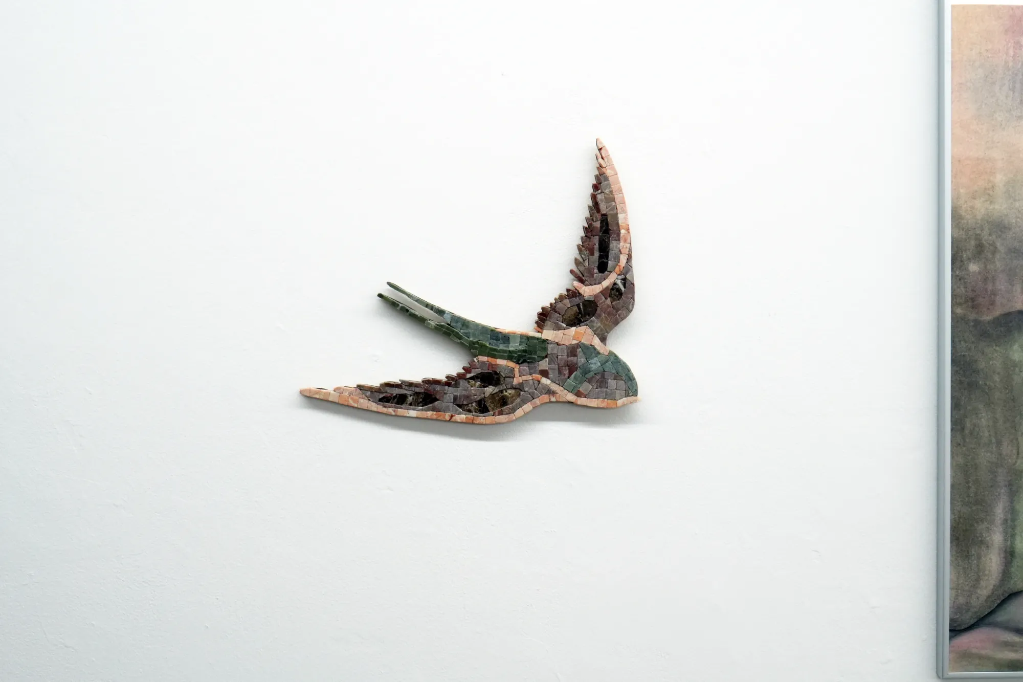 Gvantsa Jishkariani, Caramel Cutie, 2026 — wall-mounted mosaic swallow in flight, composed of marble tiles in soft beige, brown, and muted green tones, with a slender elongated tail and upward curved wing; marble mosaic on wood; The Why Not Gallery at Fabrika Project Space, Tbilisi.