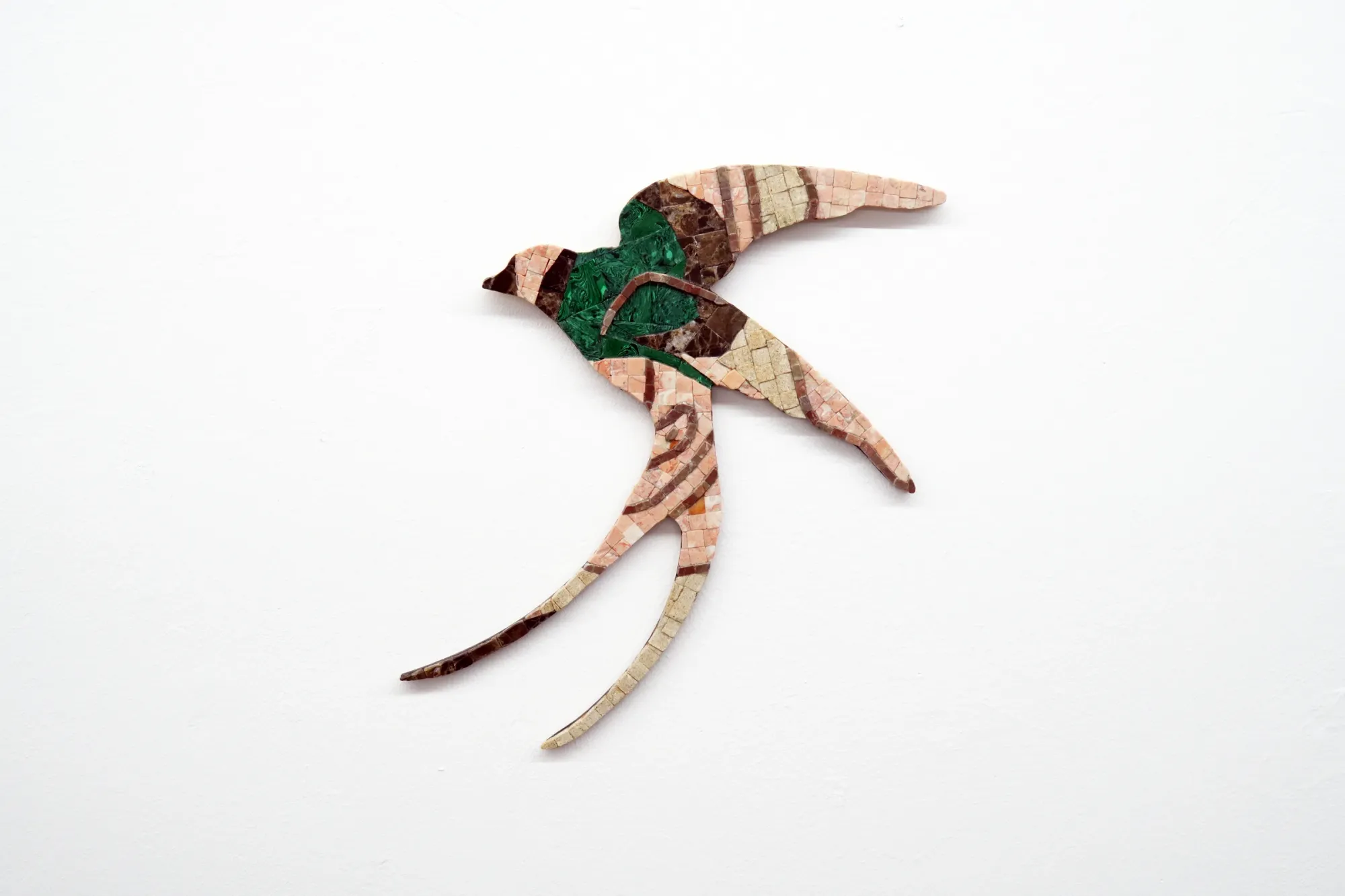 Gvantsa Jishkariani, Curious Gangster, 2026 — wall-mounted mosaic swallow in diving flight, composed of marble and beach glass tiles in pink-salmon, brown, and a vivid malachite-green chest, with long curved tail streamers; The Why Not Gallery at Fabrika Project Space, Tbilisi