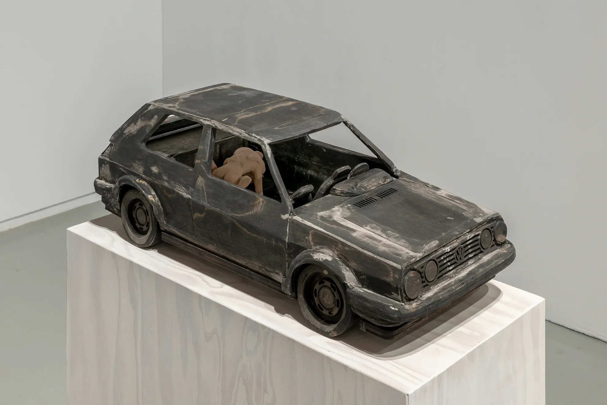 Joan Pallé, Els joves infeliços / Unhappy Youth, detail: blackened sculpture of a VW Golf GTI on a white plinth, with a small crouching human figure trapped inside the car, Centre d'Art La Panera, Lleida, 2026.