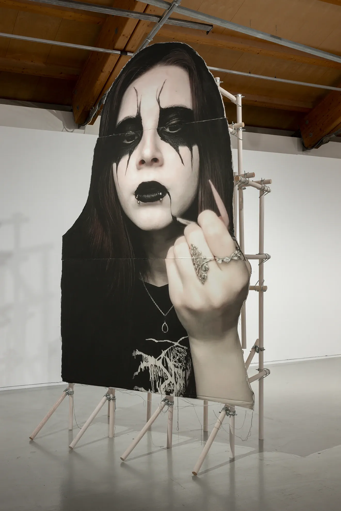 Joan Pallé, Els joves infeliços / Unhappy Youth, detail: monumental black-and-white photograph of a young woman in black metal makeup giving the middle finger, mounted on raw wooden scaffolding, Centre d'Art La Panera, Lleida