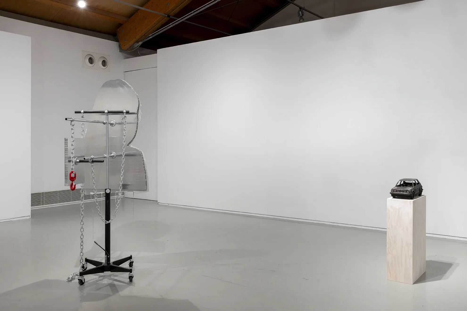 Joan Pallé, Els joves infeliços / Unhappy Youth, detail: steel structure on industrial wheels with hanging chains, red hook, and a panel reading "YOUTH" in sportswear logo format; blackened VW Golf sculpture on plinth visible in background, Centre d'Art La Panera, Lleida, 2026.