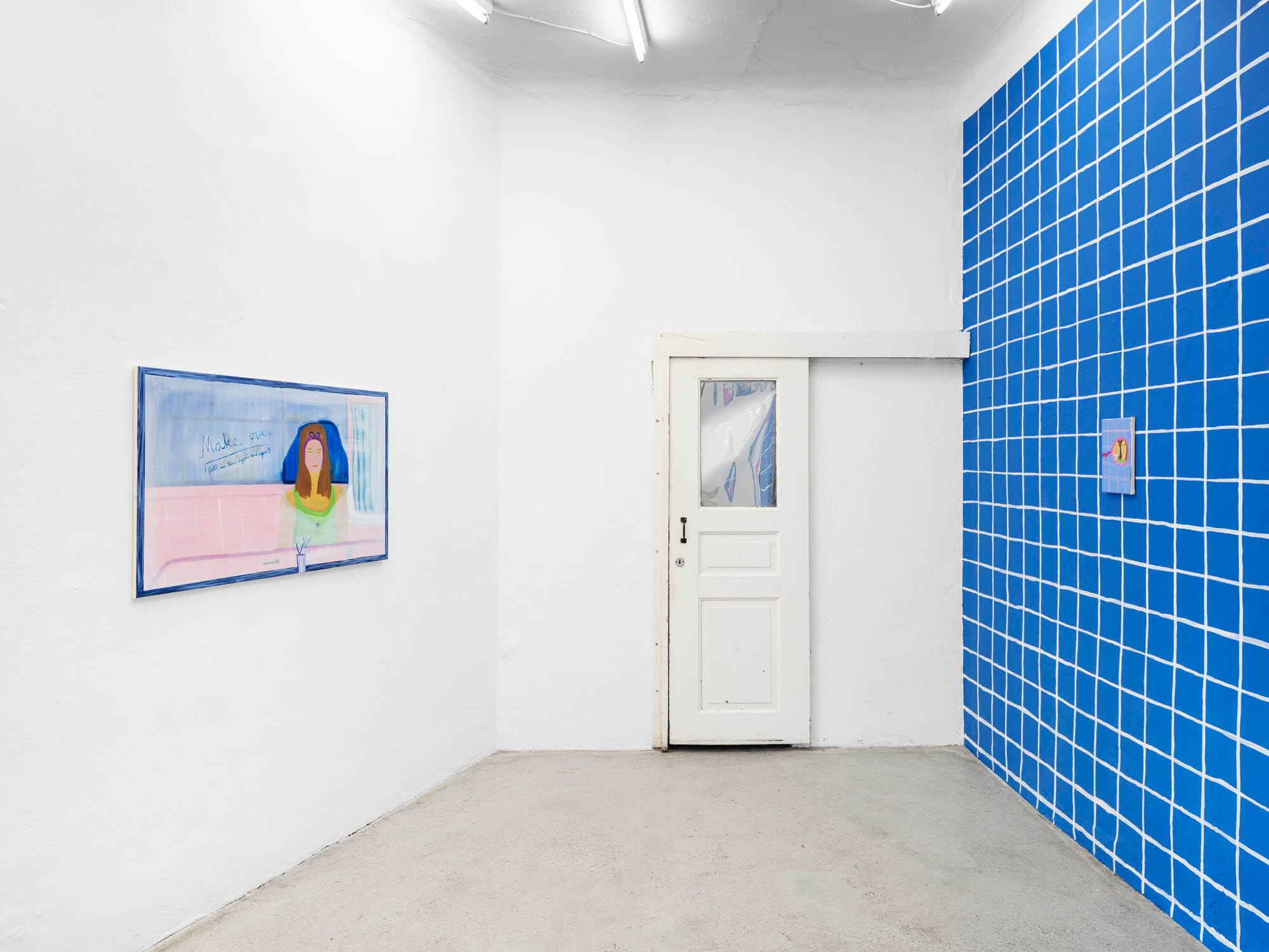 Installation view, Josefine Schulz: Makeover (fall in love again and again), Kunstraum Ortloff, Leipzig, 2026 — left wall: horizontal painting with blue frame showing woman's portrait with blue hair, handwritten text reading "Makeover / fall in love again and again", pink ground; center: white door with glass pane; right: blue tile-grid wall with small compact mirror painting.