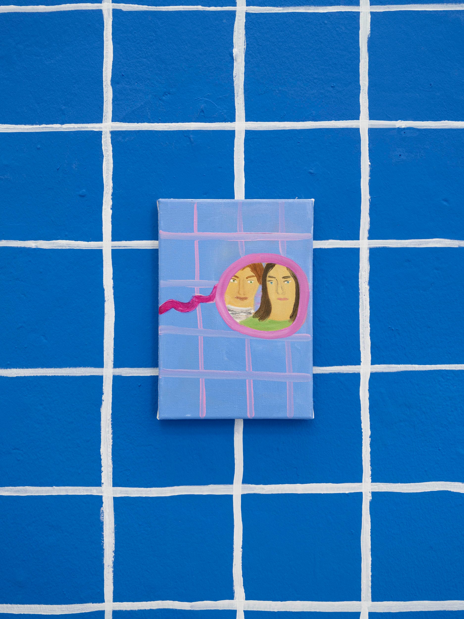 Josefine Schulz, detail view, Makeover (fall in love again and again), Kunstraum Ortloff, Leipzig, 2026 — small canvas on blue tile-grid wall depicting a pink compact mirror with curling ribbon handle; two faces side by side inside the round mirror, one with short hair and striped top, one with long dark hair and green top; light blue tile-patterned ground on canvas.