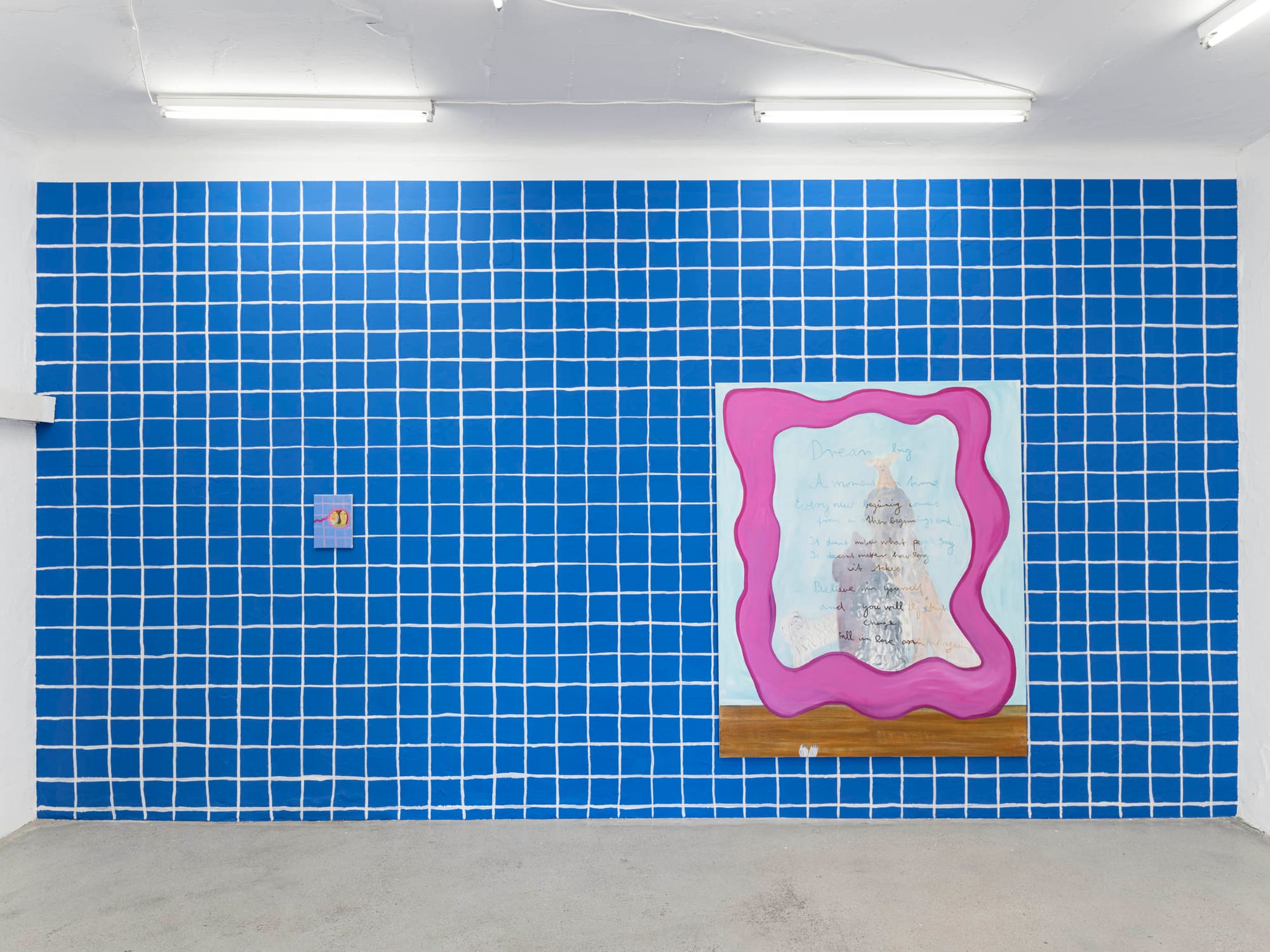 Installation view, Josefine Schulz: Makeover (fall in love again and again), Kunstraum Ortloff, Leipzig, 2026 — full frontal view of blue tile-grid painted wall; left: small compact mirror painting on tile; right: large canvas with pink-magenta wavy frame enclosing layered handwritten text and architectural motif over pale ground, wooden shelf at base.
