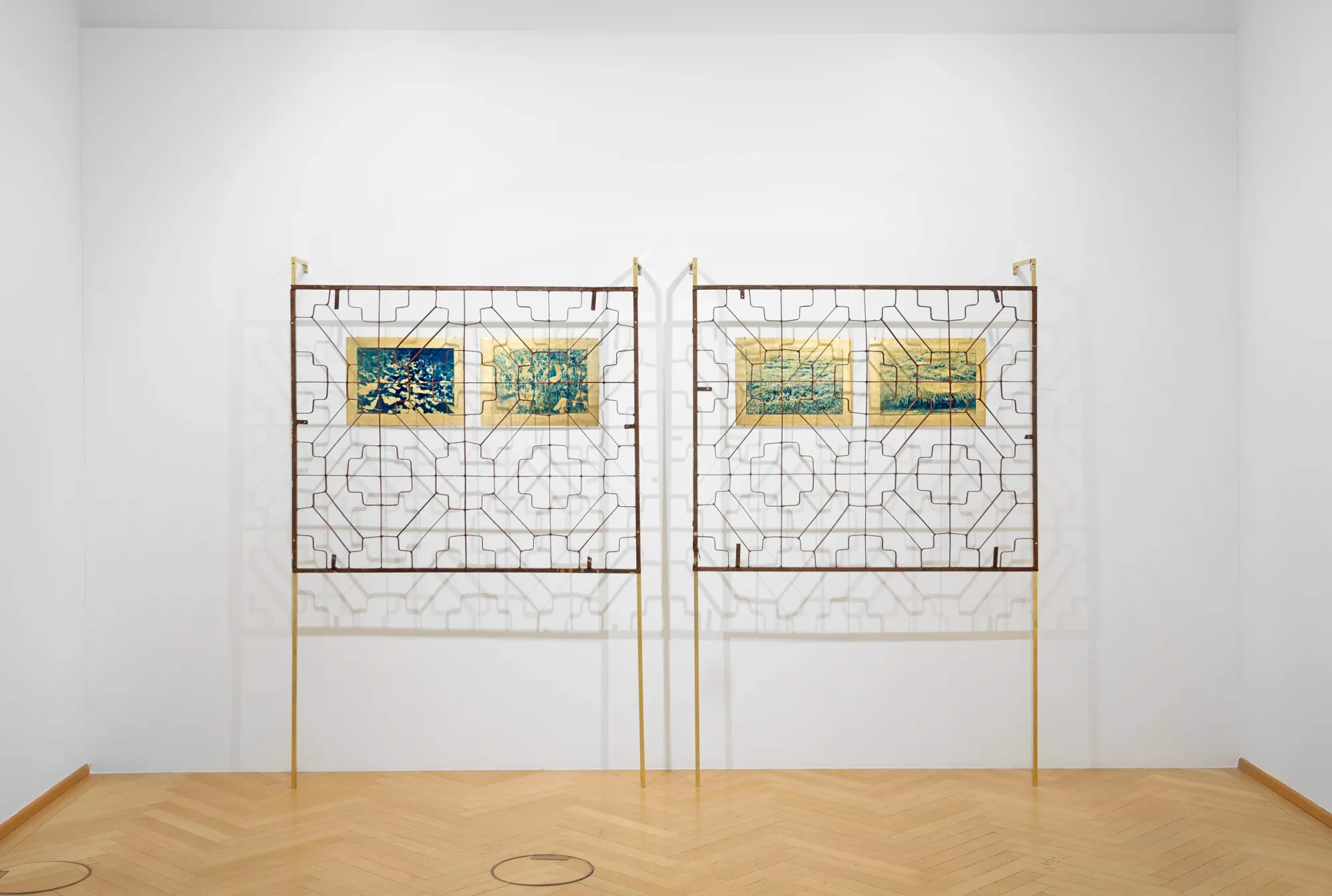 Kaja Clara Joo, 다시 : DASI, 2026, installation view. Two freestanding steel frames in Korean traditional window lattice pattern (changssal) on gold-painted legs, each holding cyanotype prints on gold latex. Korean Culture Center Vienna.