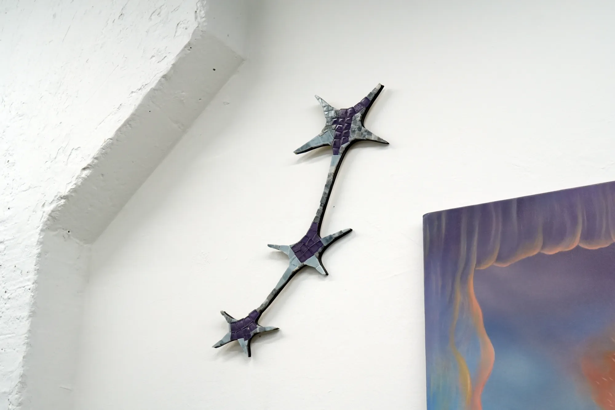 Gvantsa Jishkariani, Catalogue of galaxies n3, 2026 — wall-mounted mosaic constellation form with three star-shaped elements connected by a curved stem, composed of marble and beach glass tiles in purple and grey-green tones, installed in exhibition context; The Why Not Gallery at Fabrika Project Space, Tbilisi