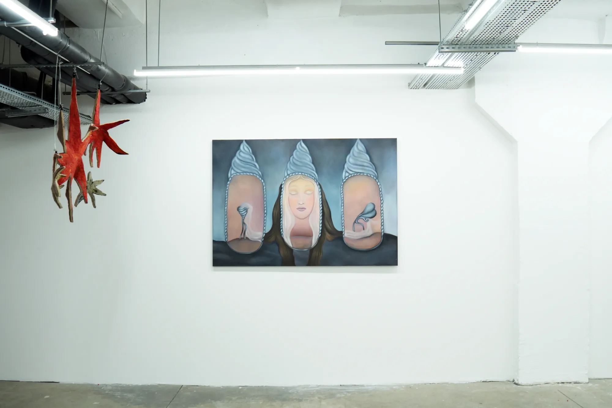Catalogue of Sensory Data, installation view — centre: Nata Varazi, Untitled, 2025, oil on canvas depicting three oval-framed figures topped with whipped cream cone forms, central female face flanked by two close-up body detail panels; upper left: Gvantsa Jishkariani, Catalogue of galaxies series, suspended felt star sculptures in red and gold; The Why Not Gallery at Fabrika Project Space, Tbilisi.