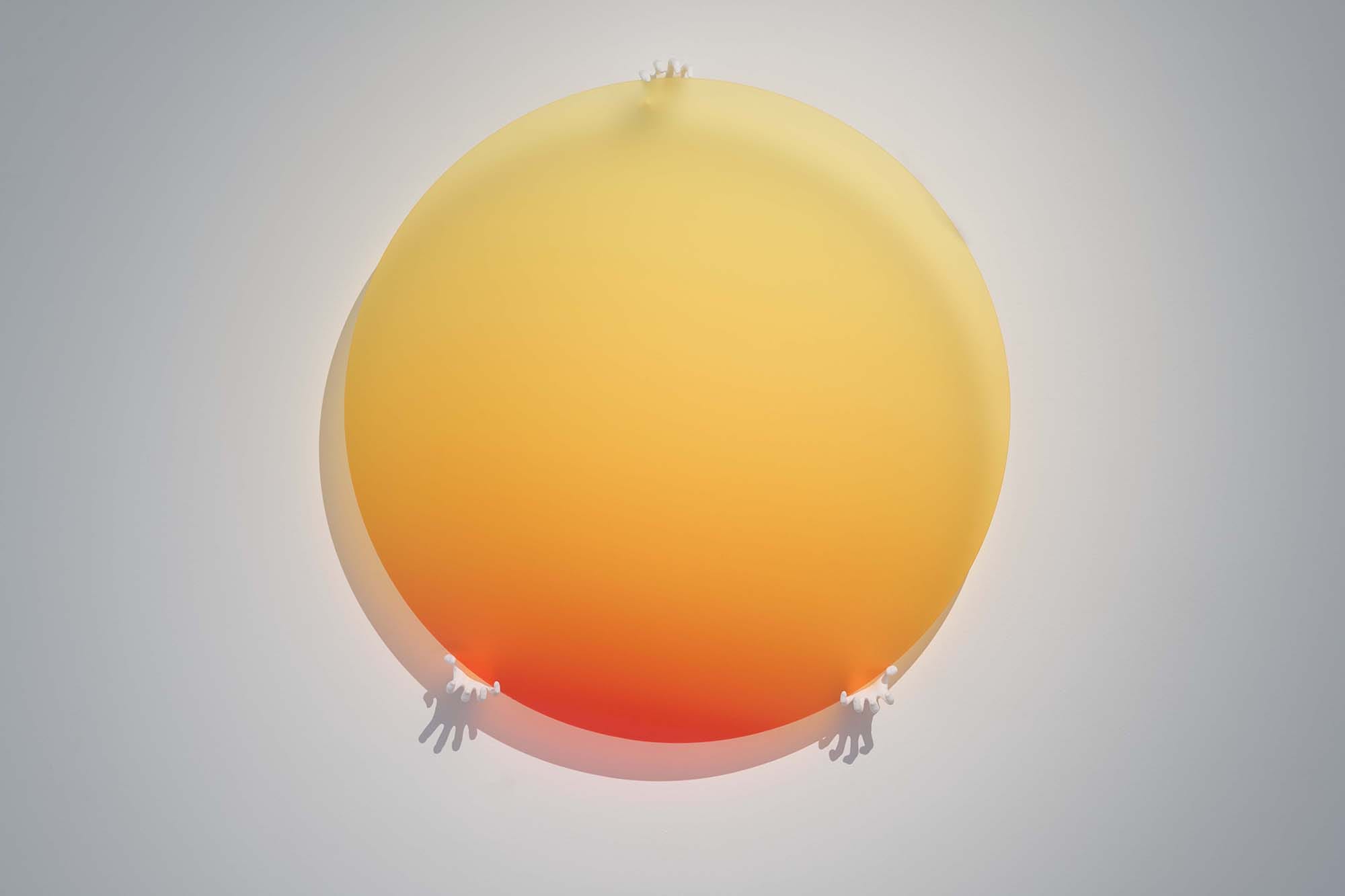 Thordis Erla Zoega, Dawn, detail: large circular gradient disc — deep orange-red at centre fading to warm yellow at rim — with two small white cast hands reaching upward from its lower edge, against a pale grey wall, BERG Contemporary, Reykjavík, 2025.