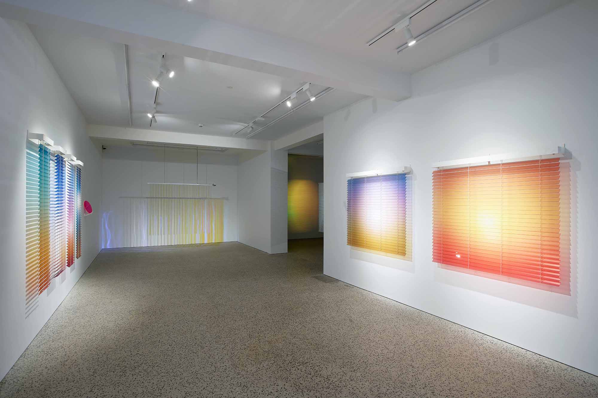 Thordis Erla Zoega, Domestic Sci-fi, installation view: second gallery room with Forecast gradient blind works on right wall and white hanging blind panels at rear; adjacent room visible through doorway with Dawn — large orange gradient disc — partially in view, BERG Contemporary, Reykjavík, 2025.