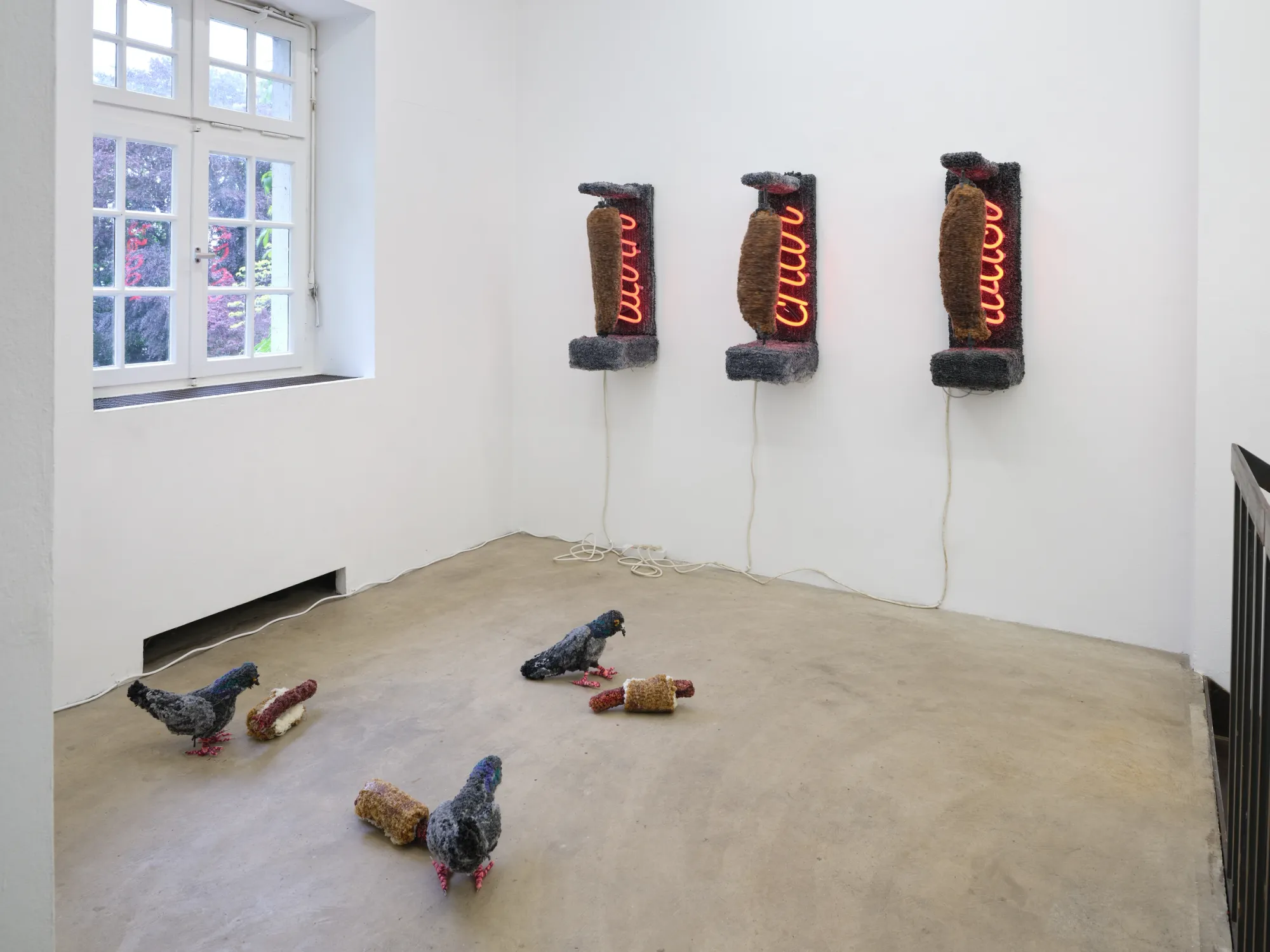 Elen Braga, Ich bin wie du, NAK Neuer Aachener Kunstverein, Aachen, 2026, three rotating textile kebab skewers with hungry pigeons on floor