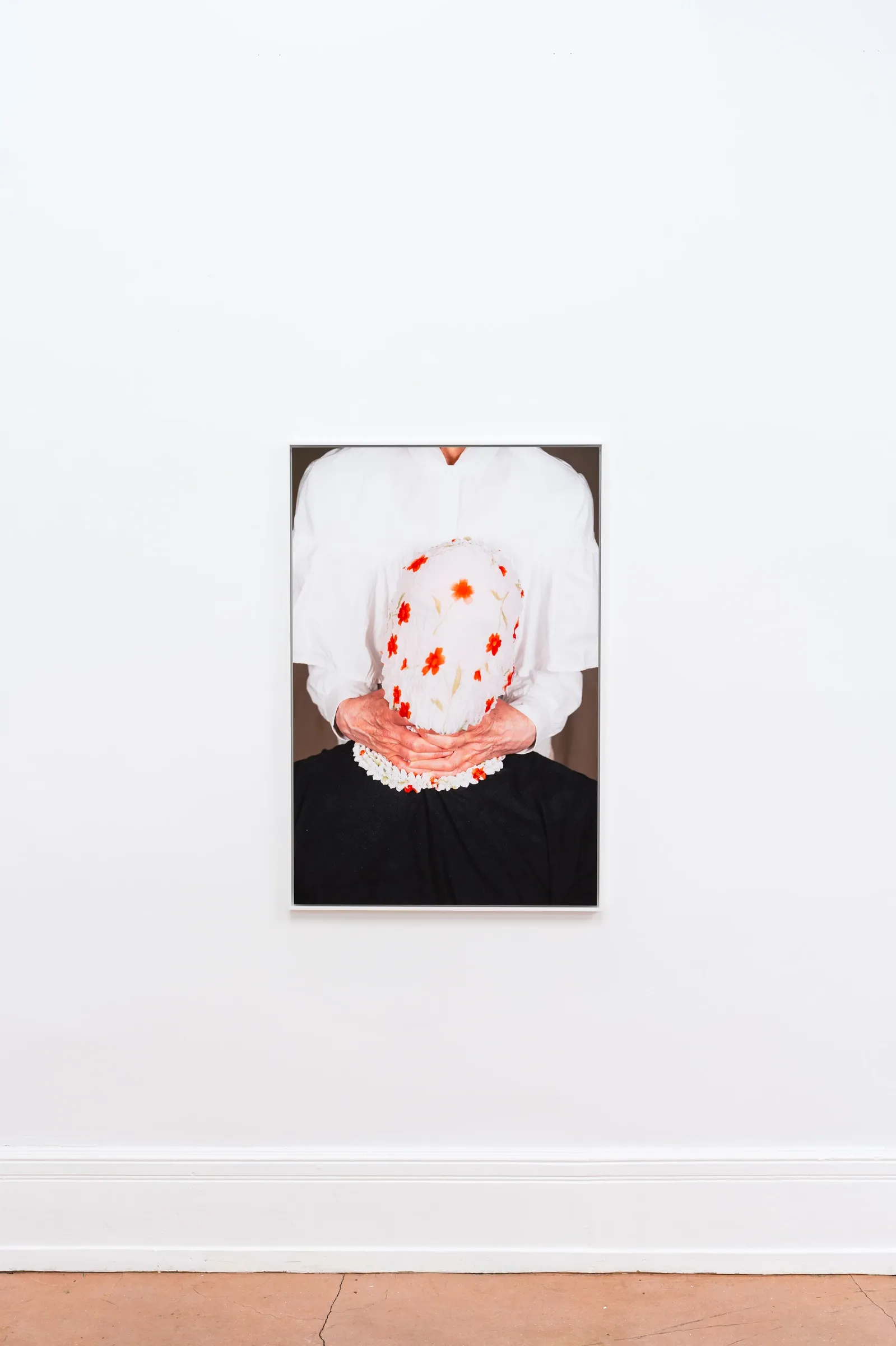 Joschua Yesni Arnaut, ungerne, Galerie 3AP, Frankfurt, 2026, framed photograph on white wall, figure with floral cloth pressed over head