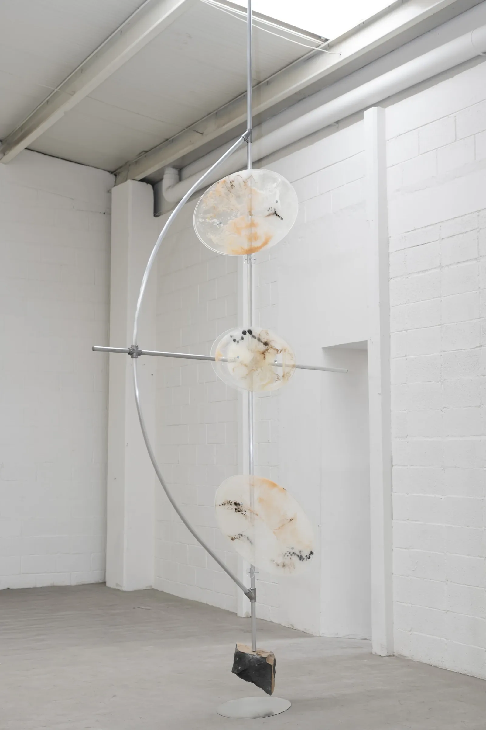 Sara Kieffer & Lucien Woodtli KiefferWoodtli, Pendulum, AXES, Alvarez Chida, Mexico City, 2026, three resin discs on vertical axis with metal arc and volcanic stone base