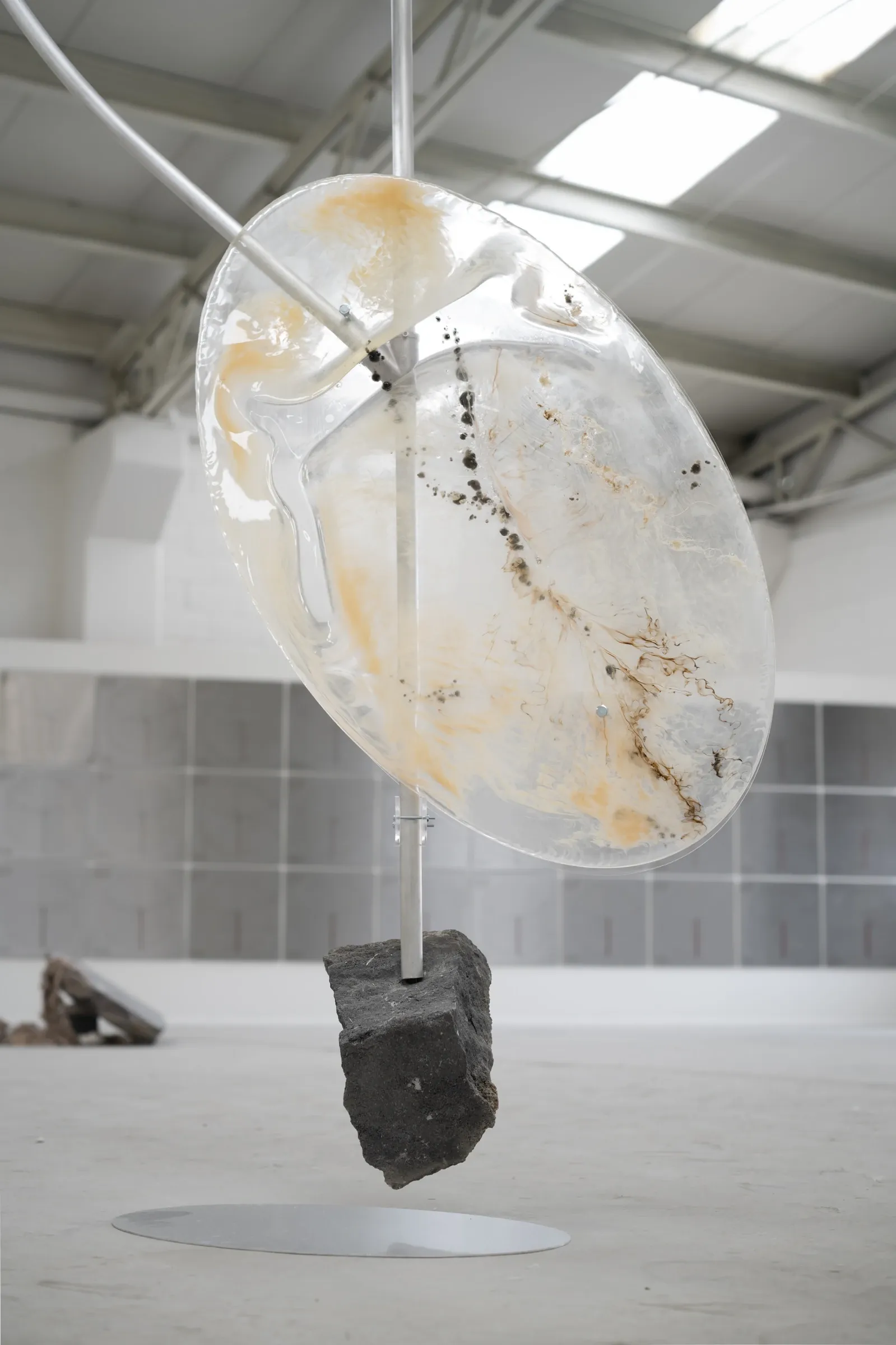 KiefferWoodtli, Pendulum, AXES, Alvarez Chida, Mexico City, 2026, translucent resin disc with amber inclusions and volcanic stone base close-up