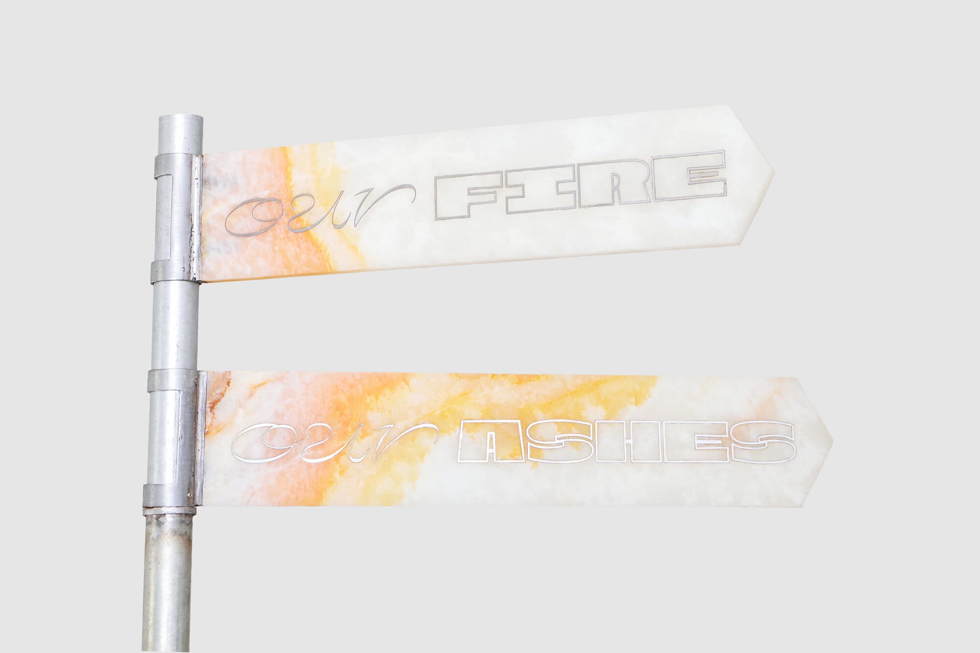 lom-of-LaMa, street-sign sculpture with two arrow-shaped panels reading "our FIRE" and "our ASHES" in mixed script, translucent marble-like material with orange-gold coloring, mounted on industrial steel post, Call Me We, 2026