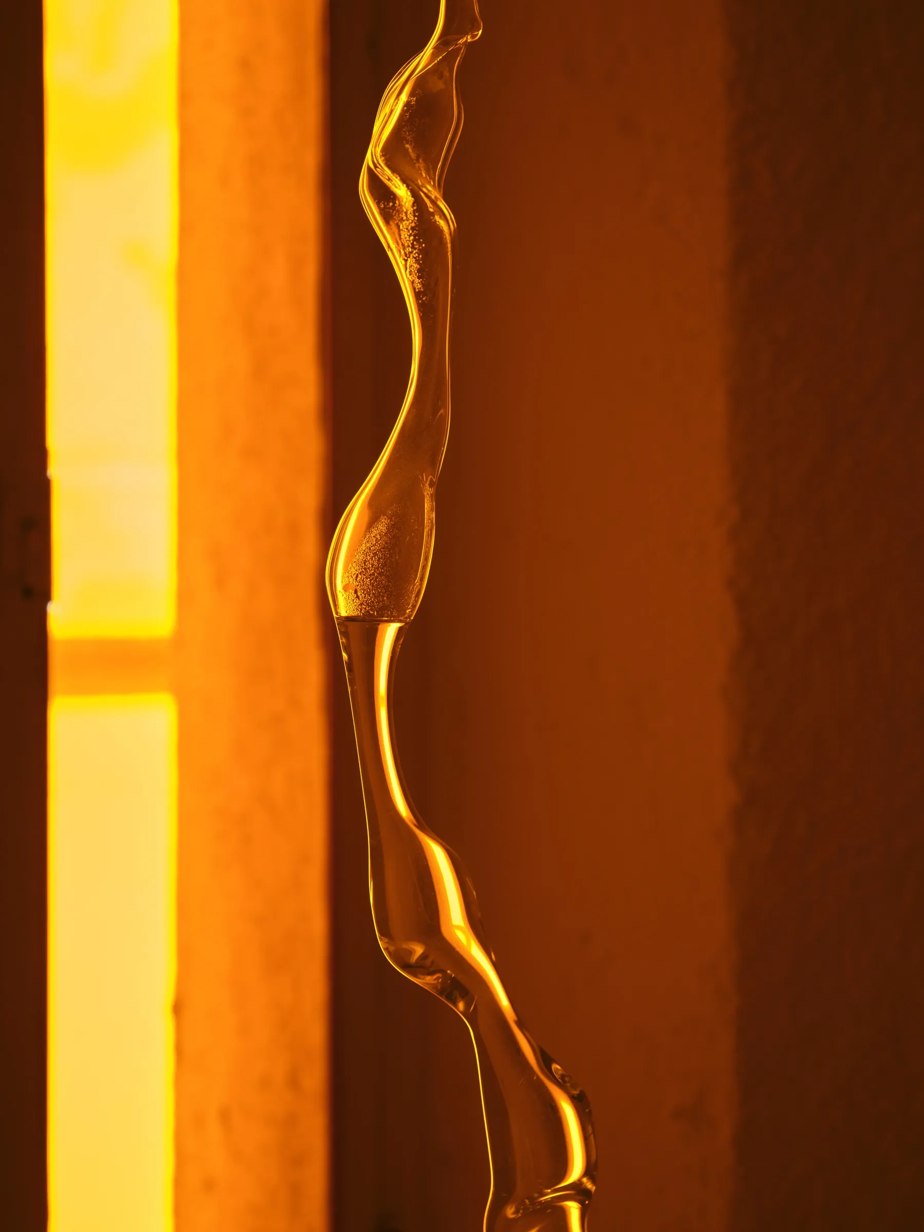Rahel Oberhummer, Sentinels, close detail of contorted glass rod glowing amber against orange-lit wall, Montreux