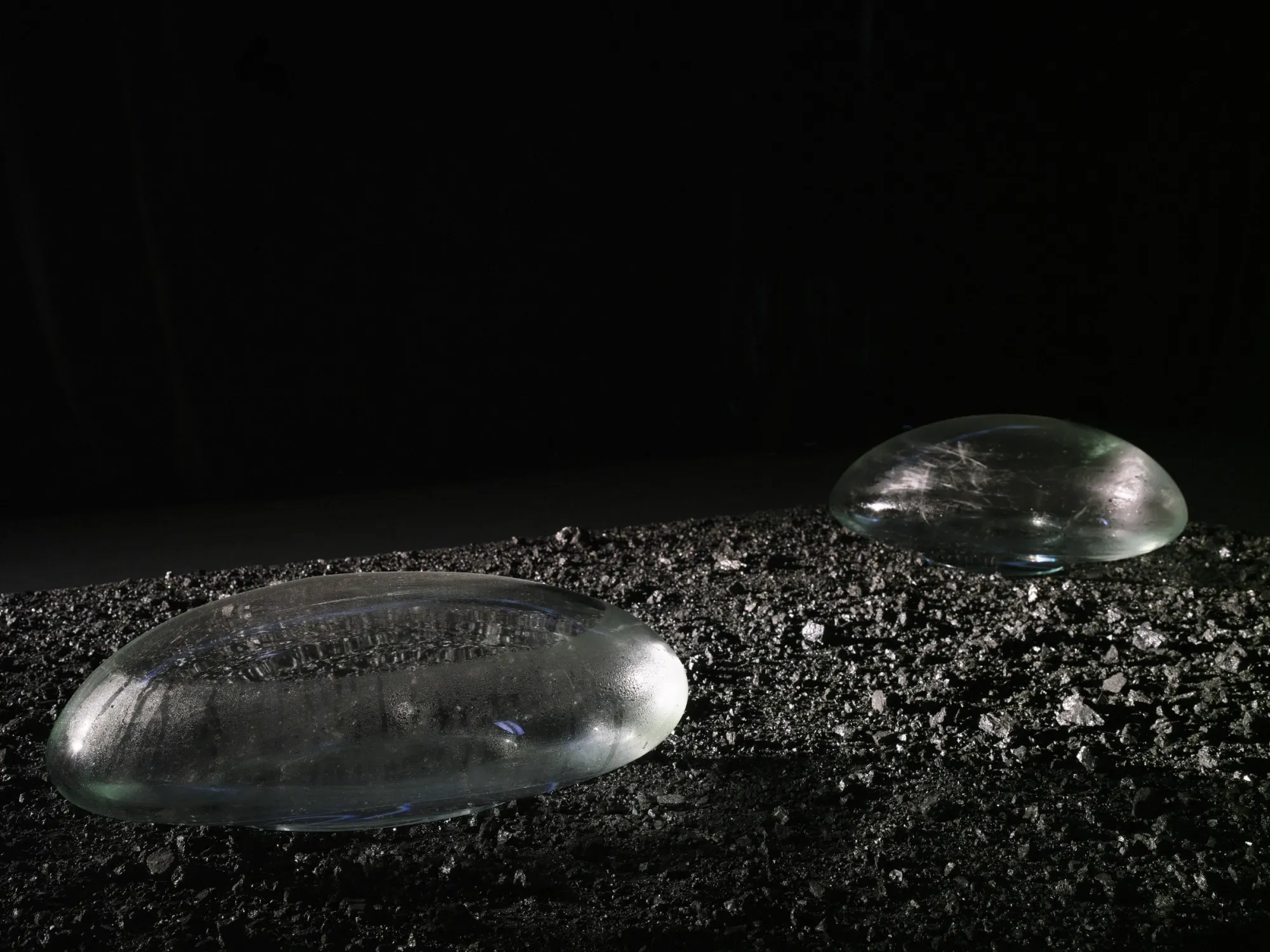 Rahel Oberhummer, Still Breathing, 2025, two glass lenses on anthracite coal, condensation visible on surface, dark background, Montreux