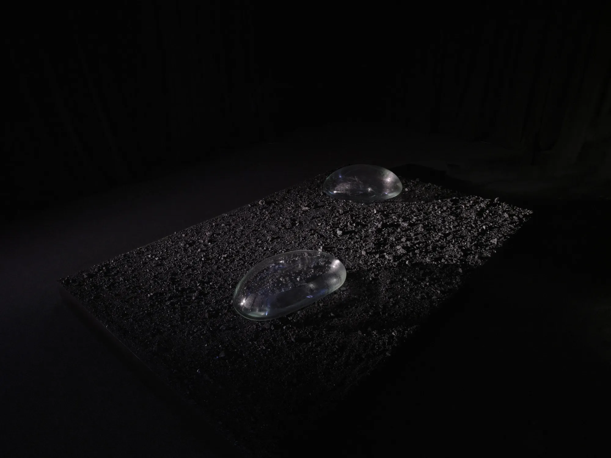 Rahel Oberhummer, Still Breathing, 2025, side-on view of glass lenses on anthracite coal, near-total black background, Montreux