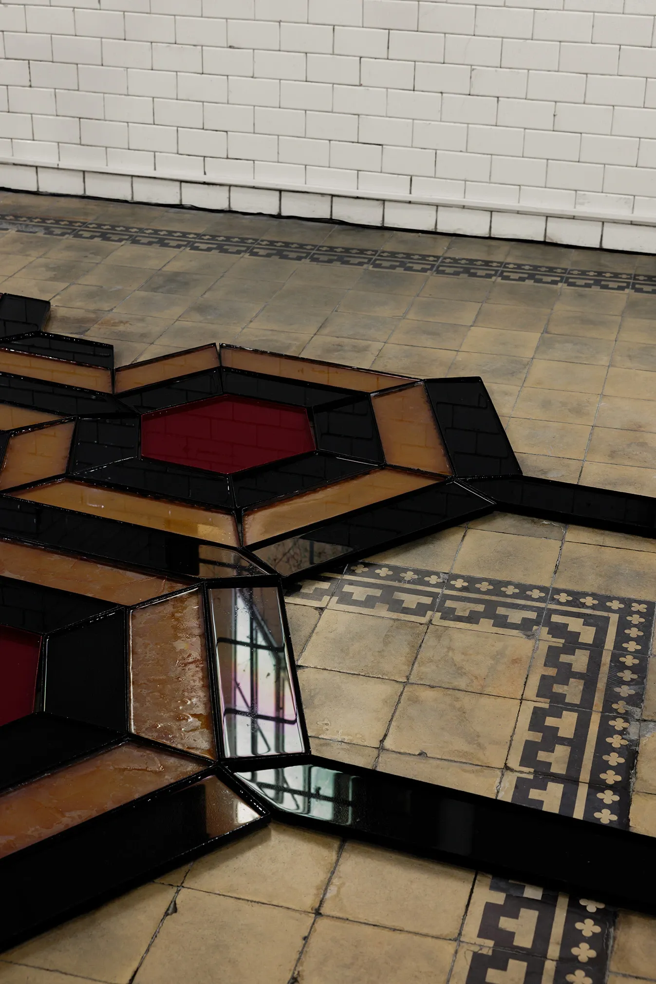Céline Struger, Echoes that refuse to fade, FAVU Gallery Brno, 2026, close-up of hexagonal glass floor modules in red amber and black with reflections