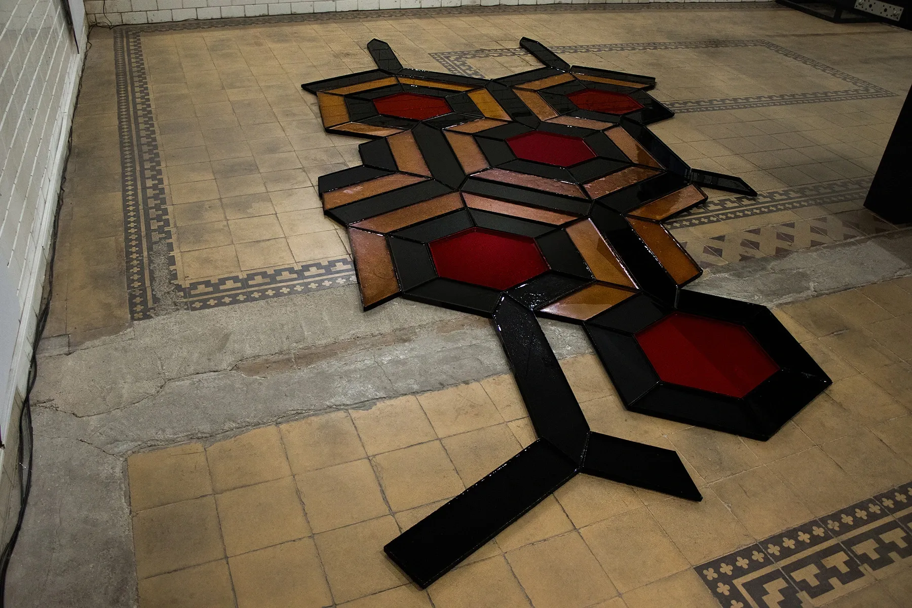 Céline Struger, Echoes that refuse to fade, FAVU Gallery Brno, 2026, modular hexagonal floor grid in red amber and black on historic tiled floor
