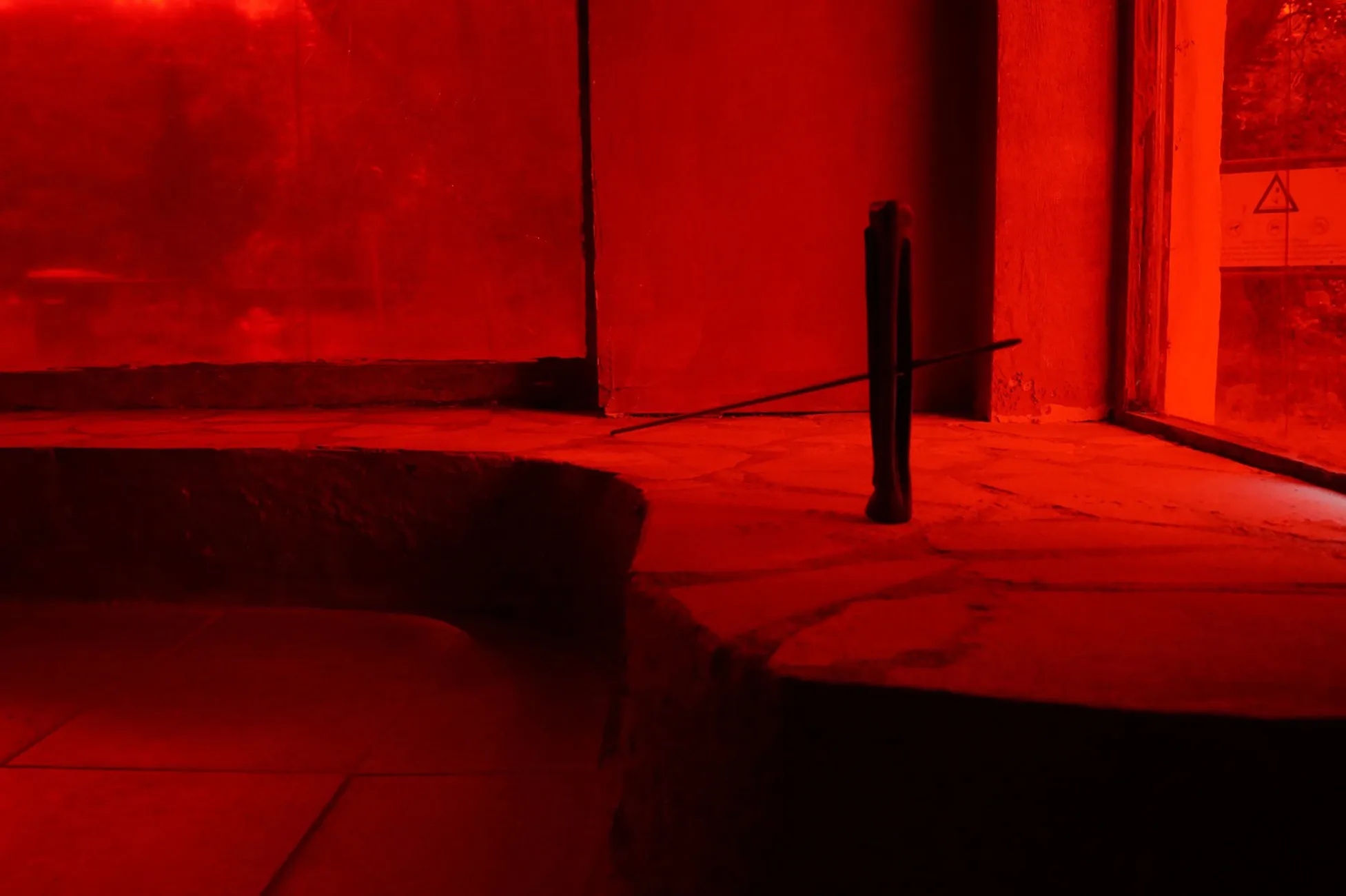 Sofiia Yesakova, Chapter II, Phantom Pförtnerhaus, Berlin, 2026, small black wood sculpture with metal rod on stone floor in red light