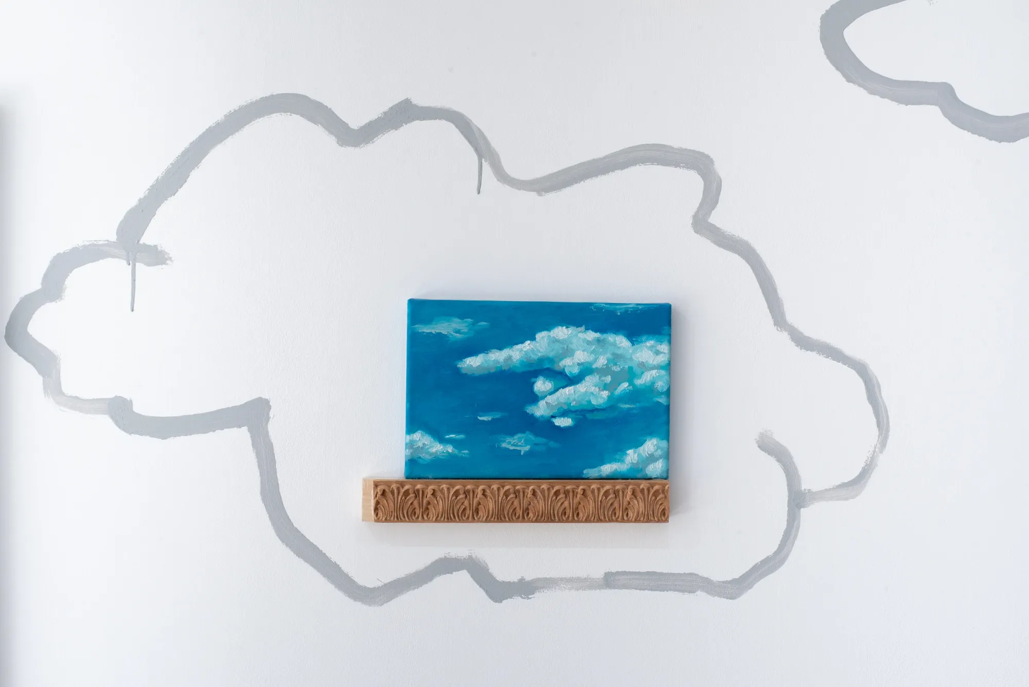 Yeti, small blue sky painting on carved decorative wooden shelf with painted cloud outline on surrounding gallery wall, The Edit Gallery, Limassol, 2026