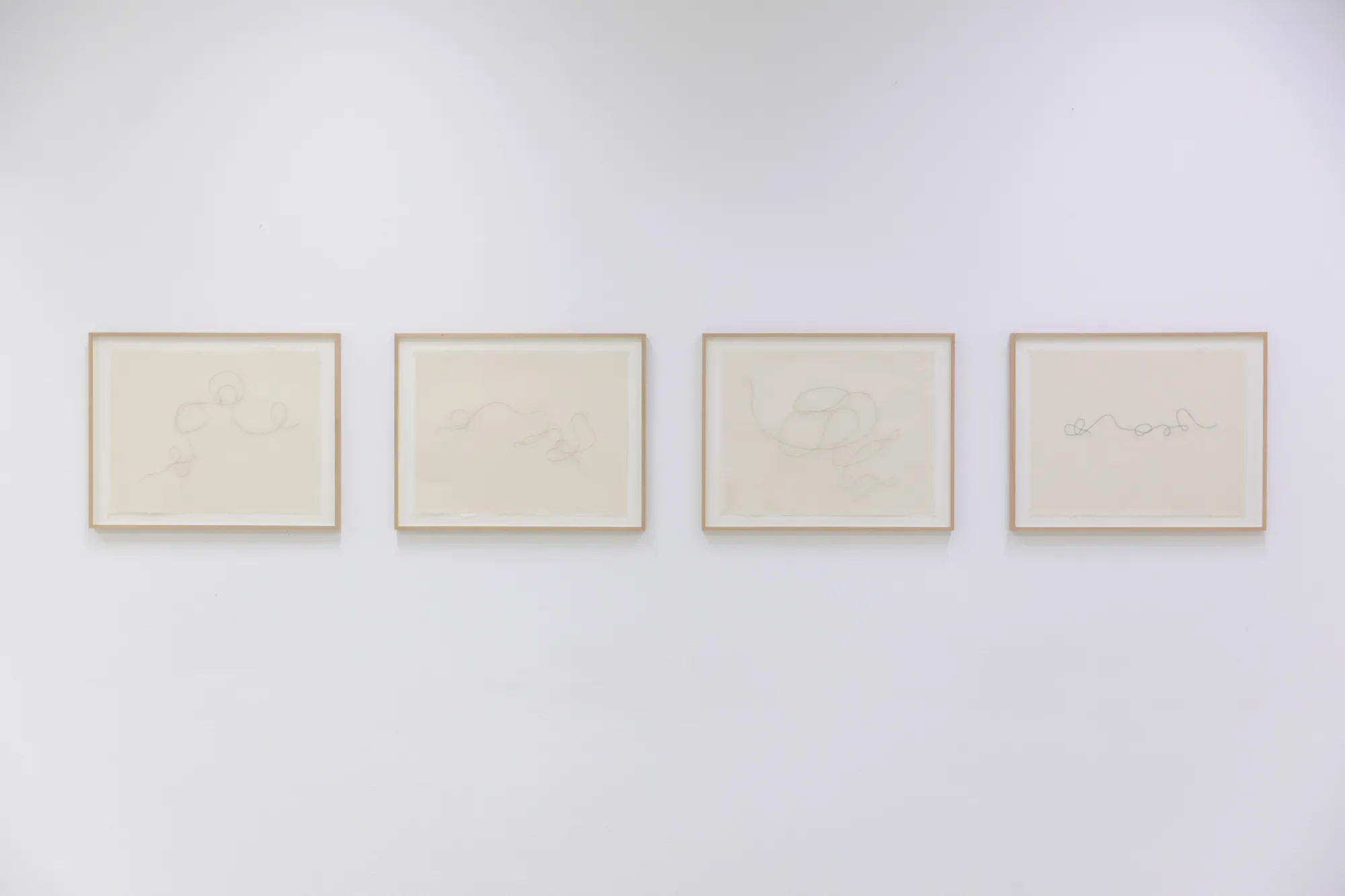Four pale framed works with delicate stitched linear forms displayed in a row on a white wall.