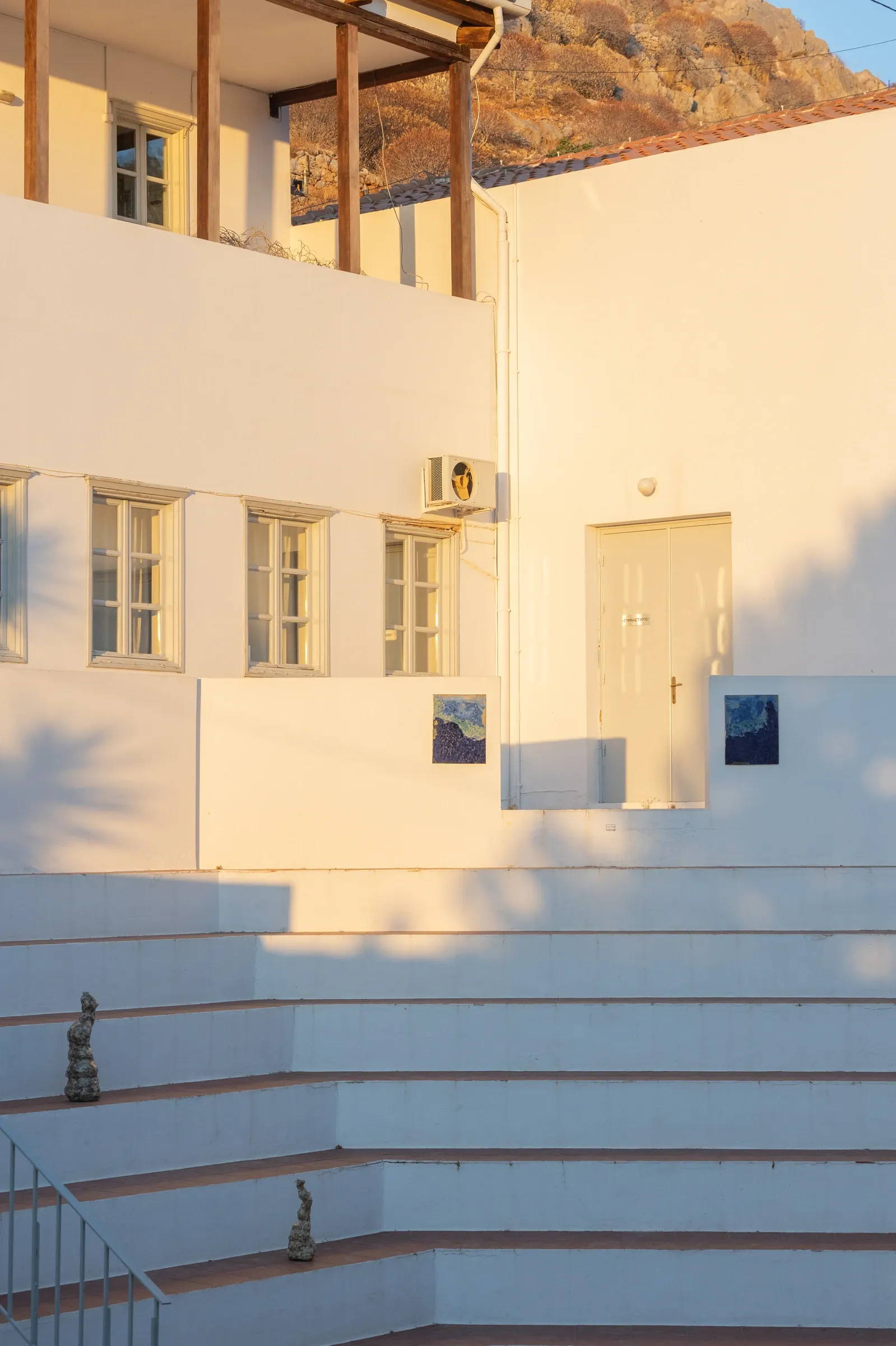 Exhibition review of Despina Charitonidi, installation view, ceramic totem sculptures on white steps beside the school facade, Hydra, 2026.