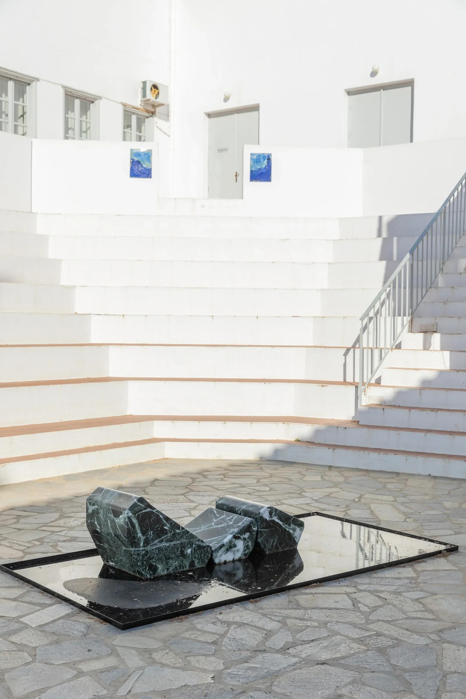 Exhibition review of Dimitrios Antonitsis, exterior facade of the former school building at golden hour with small sculptures on the steps.