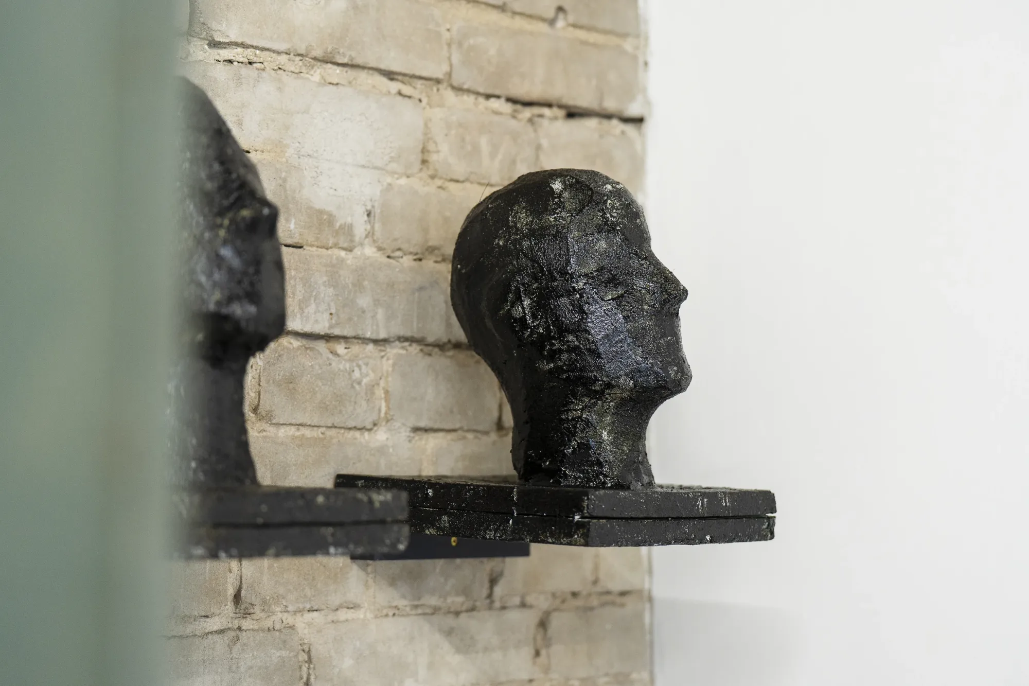 Artist Profile Feature: Erekle Chinchilakashvili, studio practice and artwork at tranzit.hu, Budapest, 2025. Close-up of two dark plaster head sculptures mounted on a wall shelf against exposed brick.