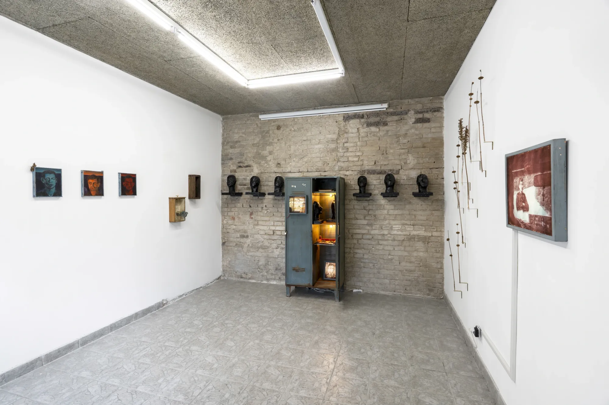 Artist Profile Feature: Erekle Chinchilakashvili, studio practice and artwork at tranzit.hu, Budapest, 2025. Brick-walled room with dark plaster heads on a wall shelf and a lit blue steel archive cabinet.