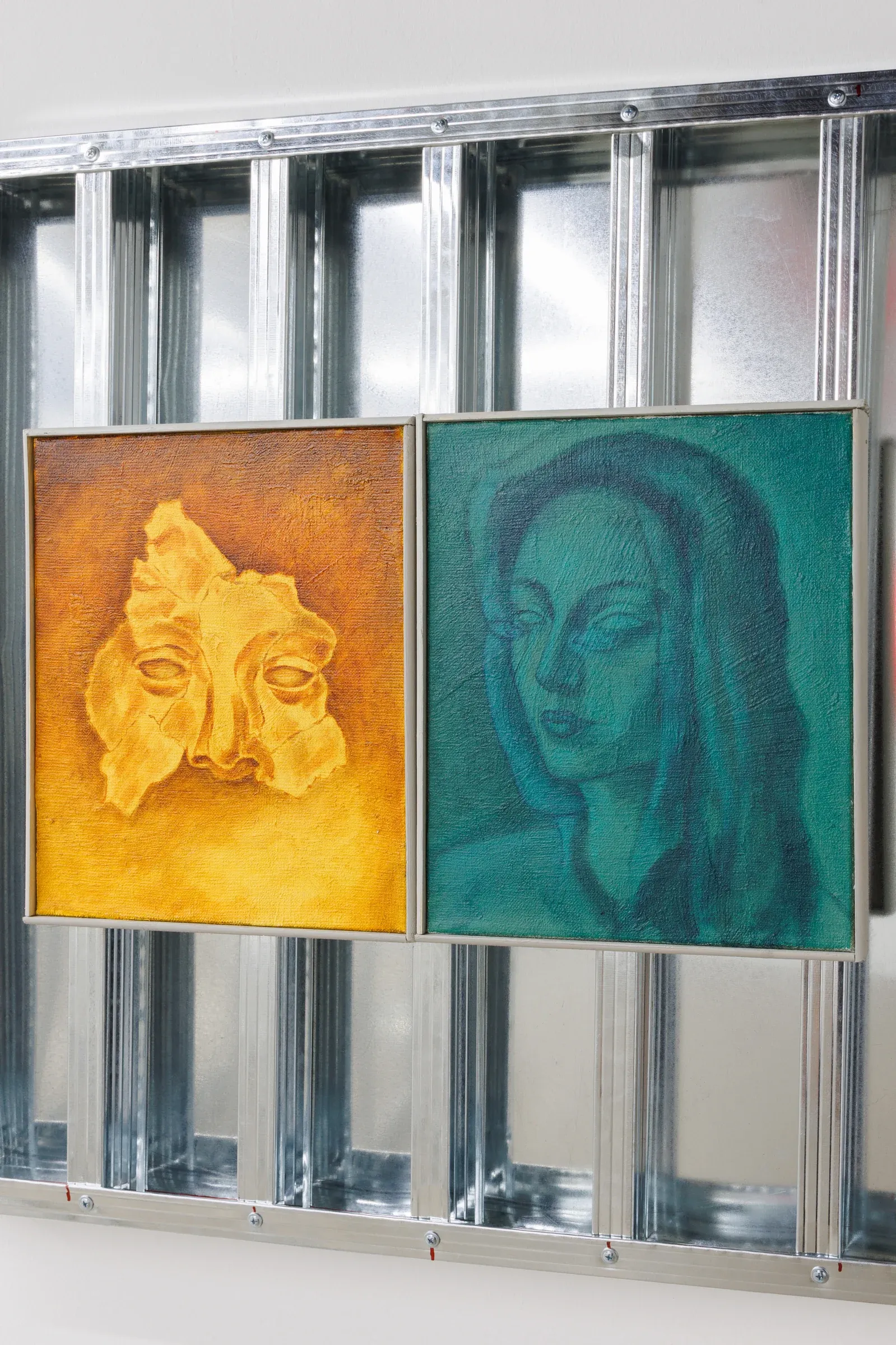 Exhibition review of Erekle Chinchilakashvili: The Story of a Thread Seen From the Window at The Why Not Gallery, Tbilisi, 2026, detail, two paintings in a shared aluminum frame, one ochre-yellow face form beside a teal-toned portrait.