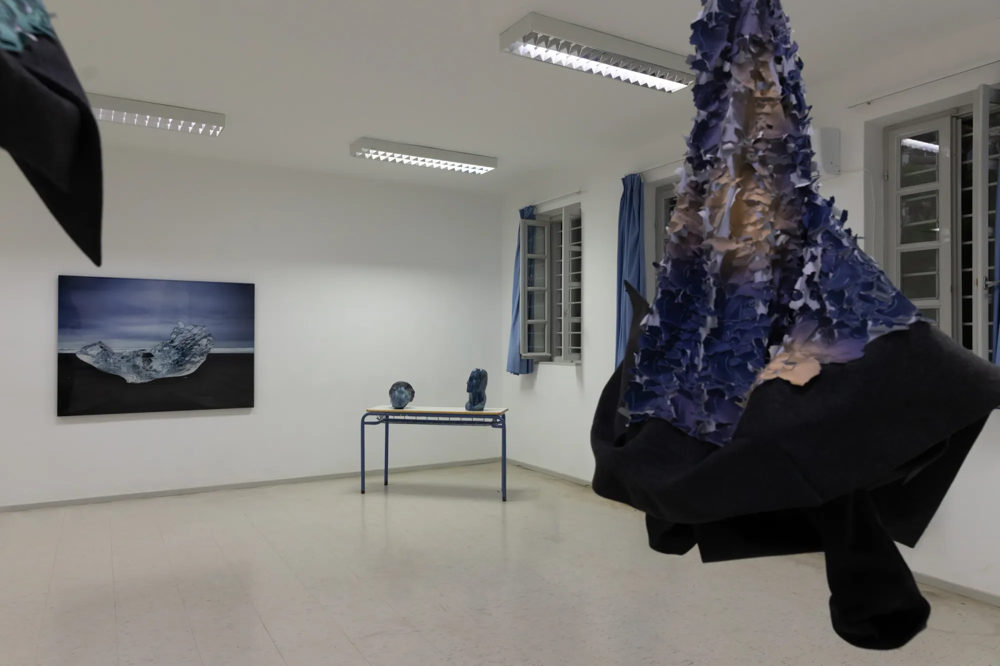 Exhibition review of Fokion Zissiadis, installation view, iceberg photograph on gallery wall beside sculpture fragments and hanging textile scales.
