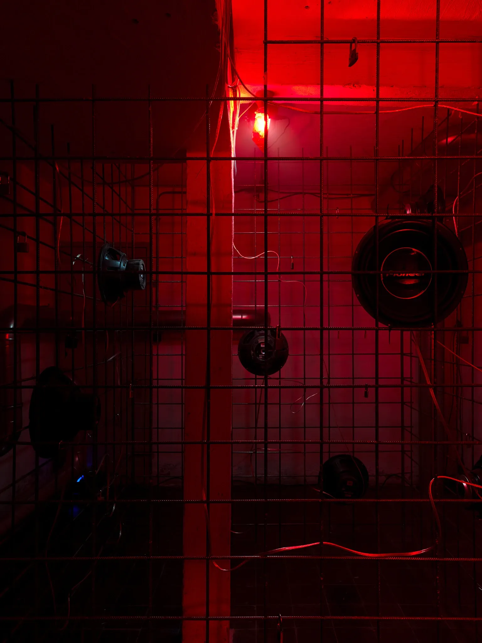Hannah Perry, Hard Love, Tick Tack, Antwerp, 2026, detail of rebar cage with padlocks and subwoofers under red light