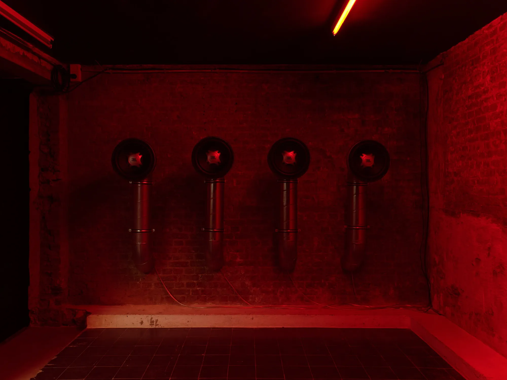 Hannah Perry, Hard Love, Tick Tack, Antwerp, 2026, red-lit basement corridor with four subwoofers mounted on brick wall