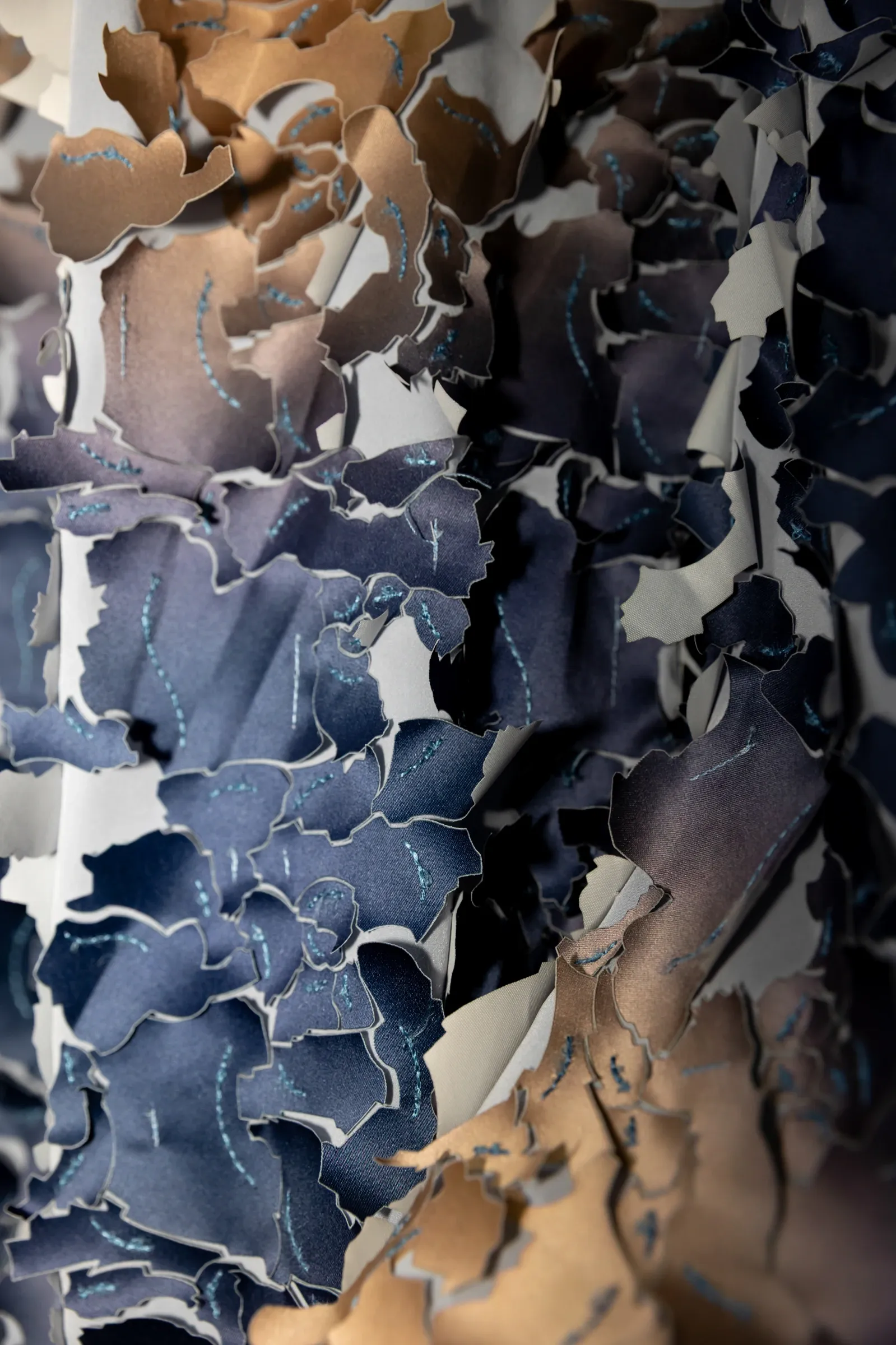 Exhibition review of Hussein Chalayan, close-up detail showing stitched fabric scales in blue, grey, and tan tones.