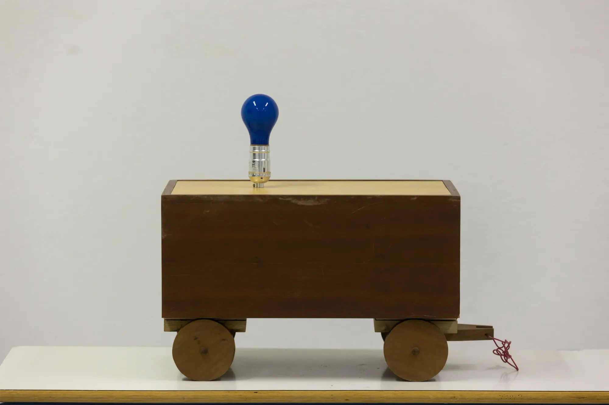 Exhibition review of Joe Bradley, boxy wooden cart assembled from found parts with a blue light bulb fixed on top, Hydra, 2026.