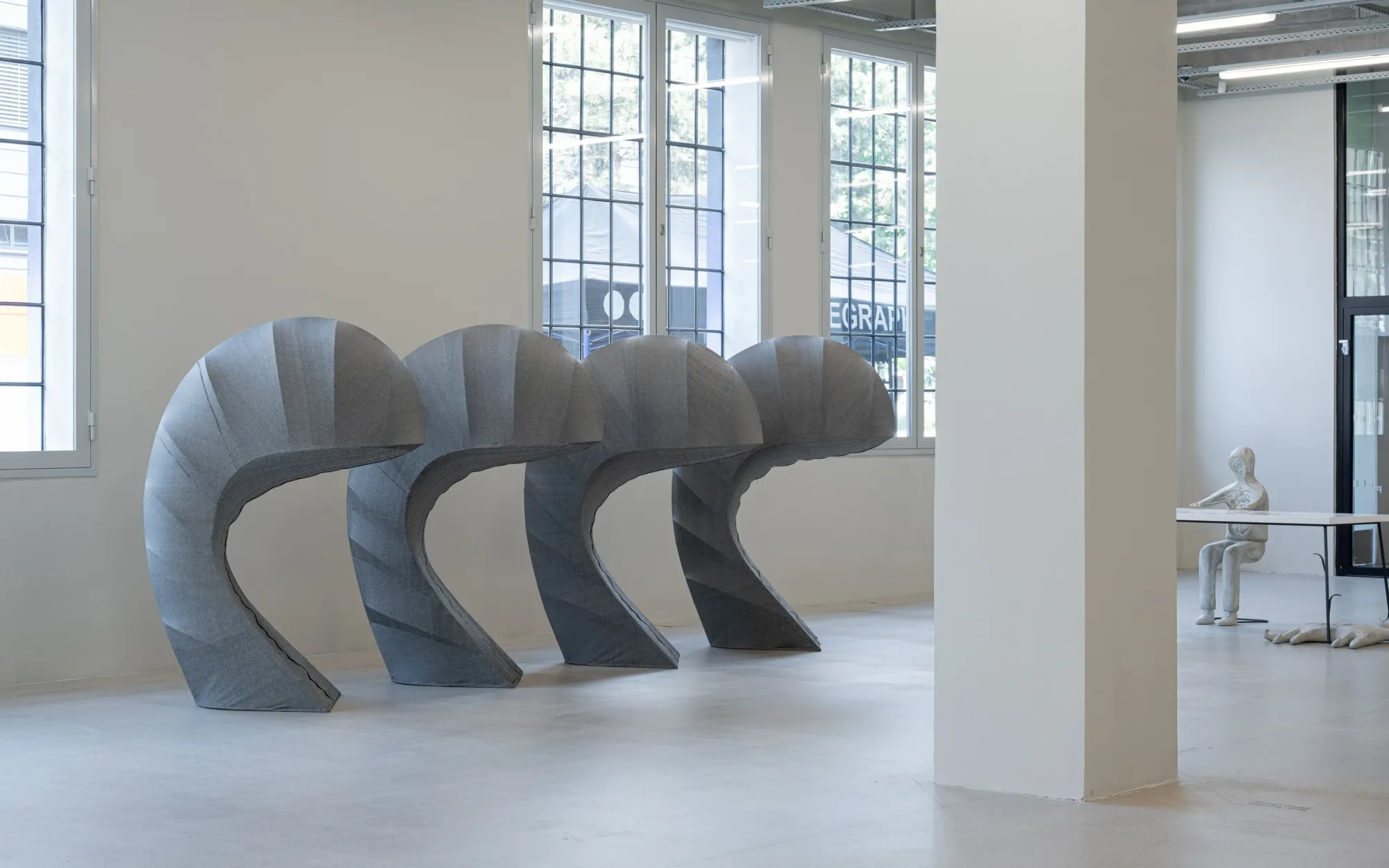 Exhibition review of Milena Dopitová: Signal V at Telegraph Gallery, Olomouc, 2026. Four grey fabric-wrapped forms bowing in a row on a concrete floor.