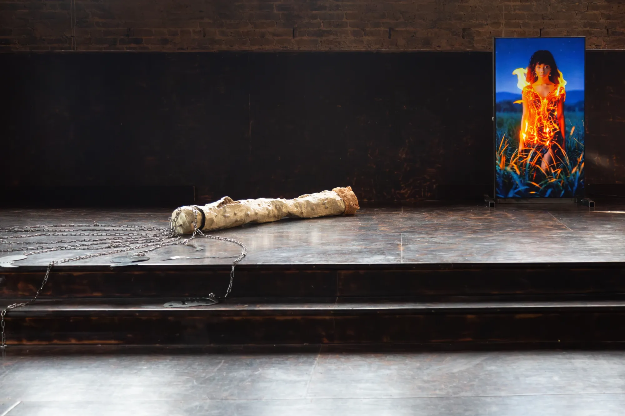 Nicola Genovese, Infinite Stage, Raleigh Chapel, London, 2026, cast limb sculpture in chains before a video screen showing a figure in flames