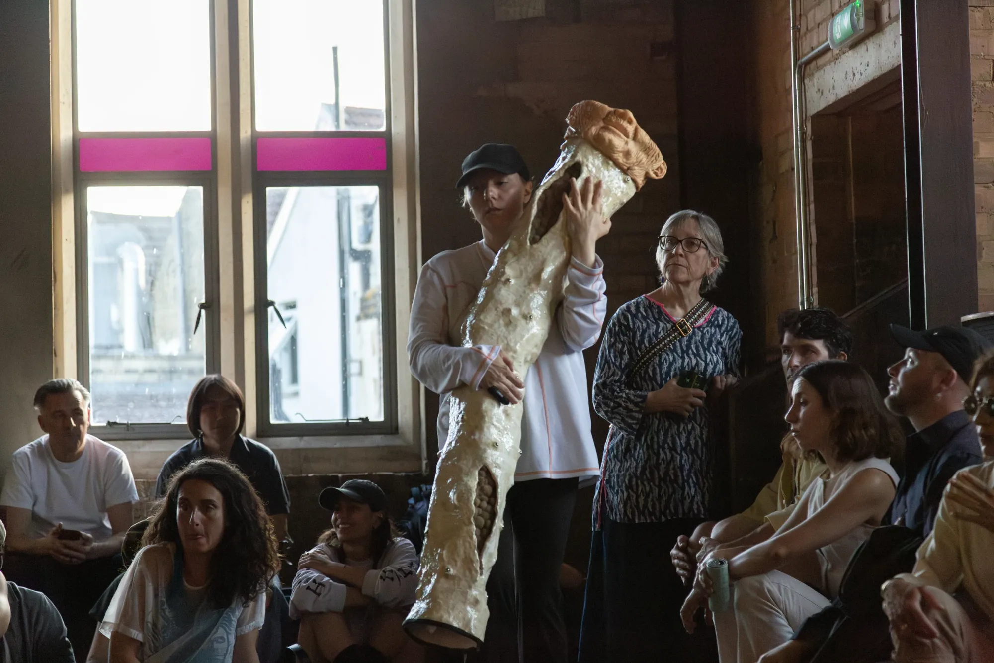 Nicola Genovese, Infinite Stage, Raleigh Chapel, London, 2026, performer carrying an upright cast sculpture past a seated audience