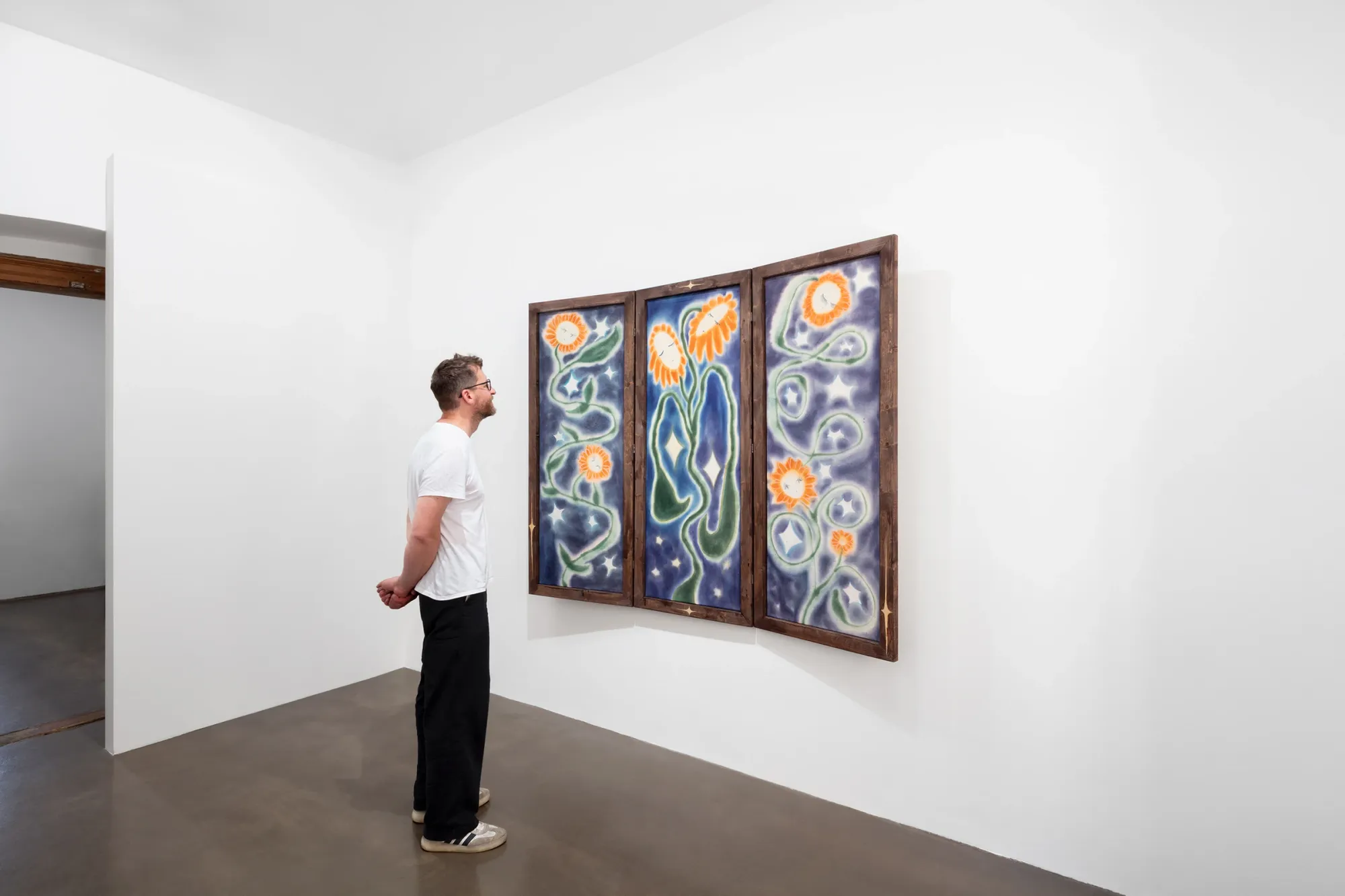 Olga Krykun, Stardust for Tomorrow, Clauda, Prague, 2026, visitor viewing a three-panel sunflower painting in a narrow room