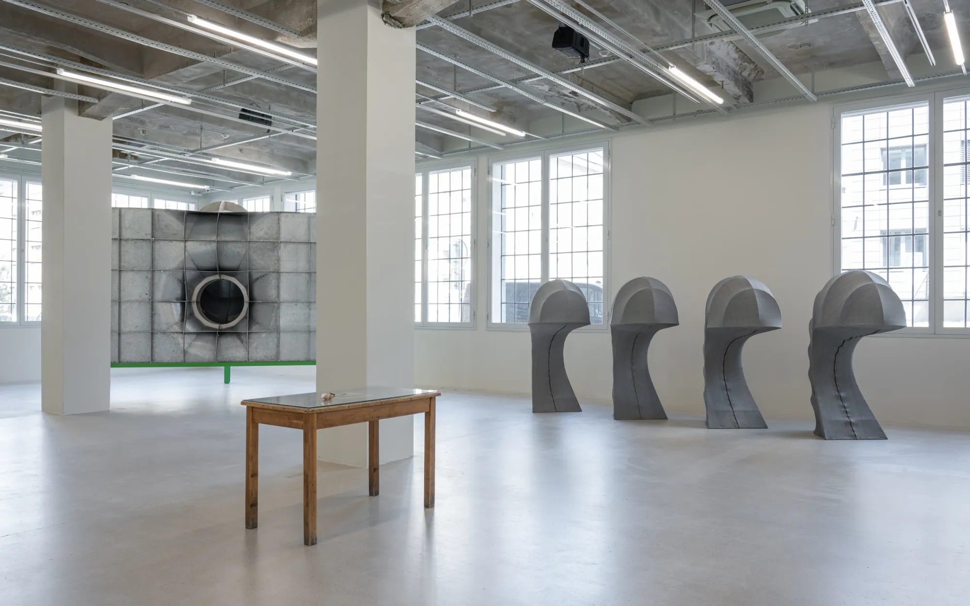 Exhibition review of Signal V at Telegraph Gallery, Olomouc, 2026. Room view with a metal panel, wooden table, and bowed fabric forms.