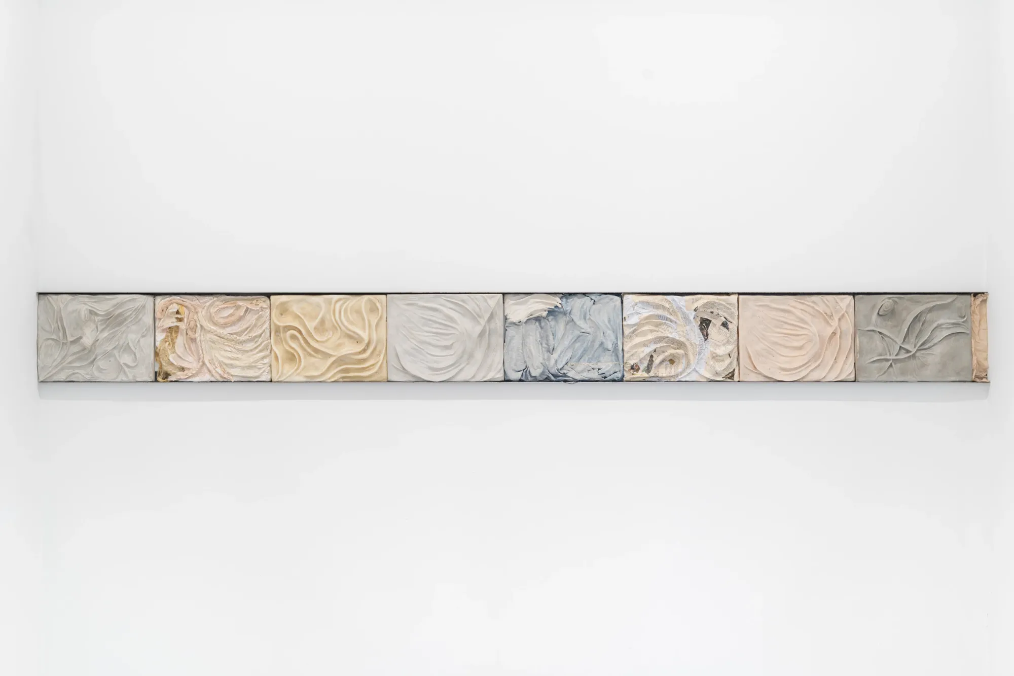 Exhibition review of Agnieszka Topolska: Call It Fate, Call It Karma at Galeria Skala, Poznań, 2026. Row of eight textured cast relief tiles including denim fabric and printed paper collage.