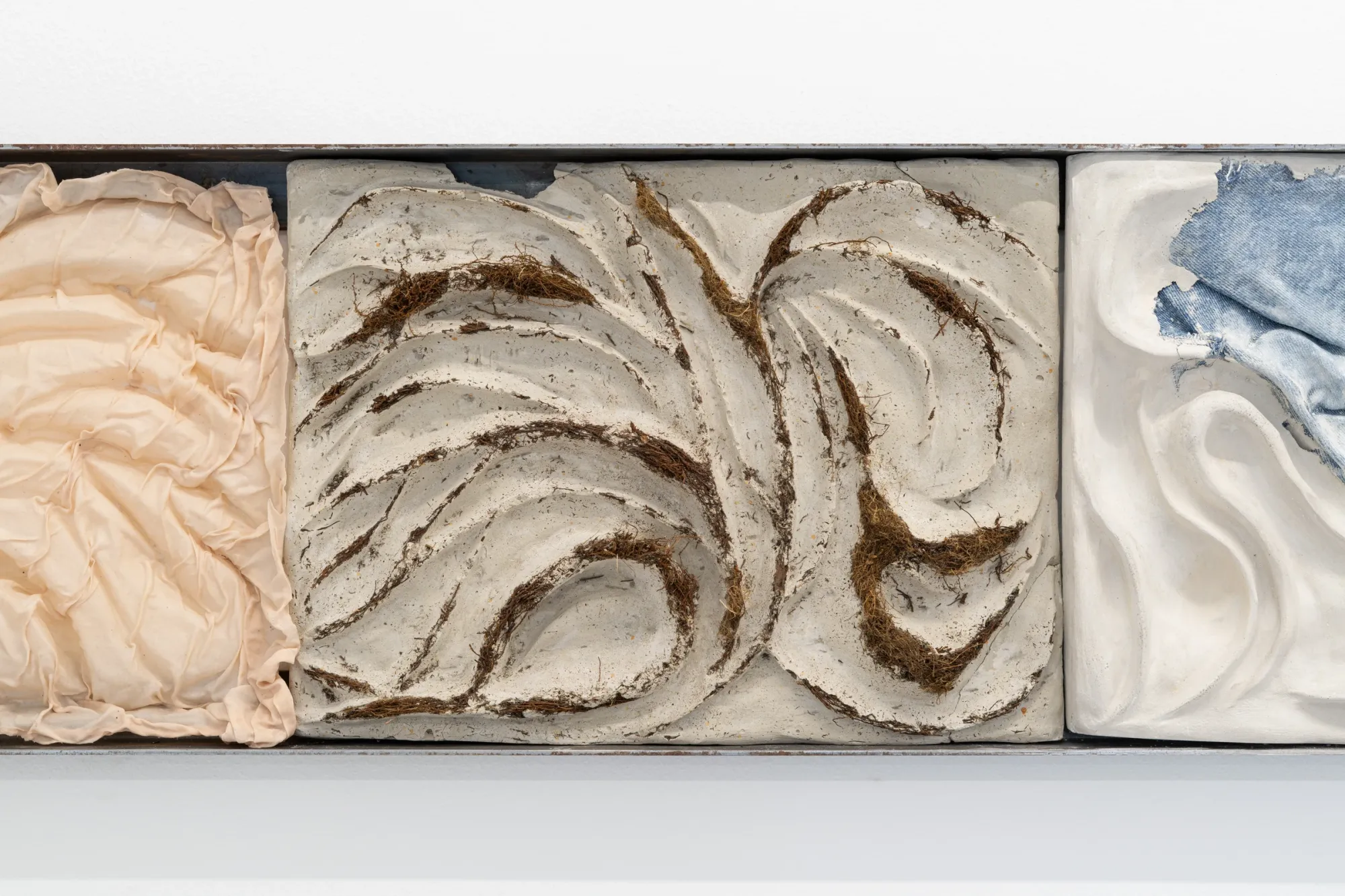 catapult contemporary exhibition review Exhibition review of Agnieszka Topolska: Call It Fate, Call It Karma at Galeria Skala, Poznań, 2026. Close-up of a relief tile with a denim fragment shaped like a map embedded in pale plaster.