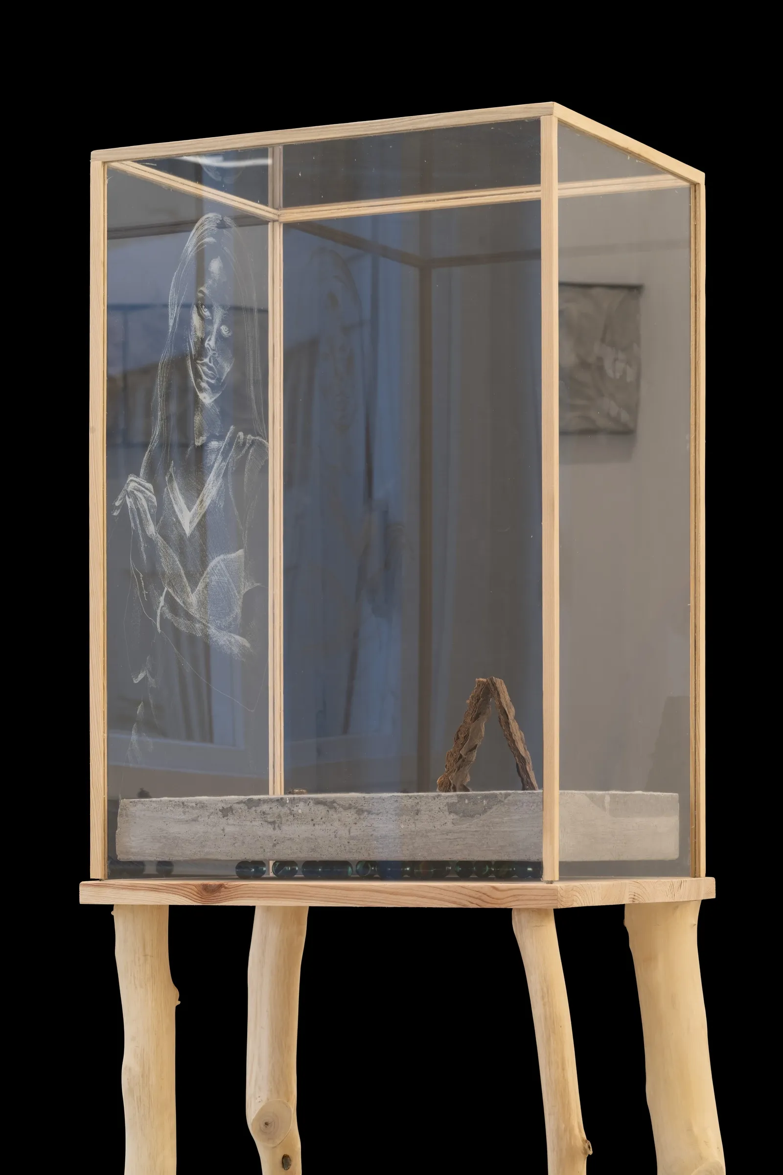 Exhibition review of Agnieszka Topolska: Call It Fate, Call It Karma at Galeria Skala, Poznań, 2026. Glass and wood display case on a black background, faint drawn figure on the glass, wood fragment on a concrete slab.