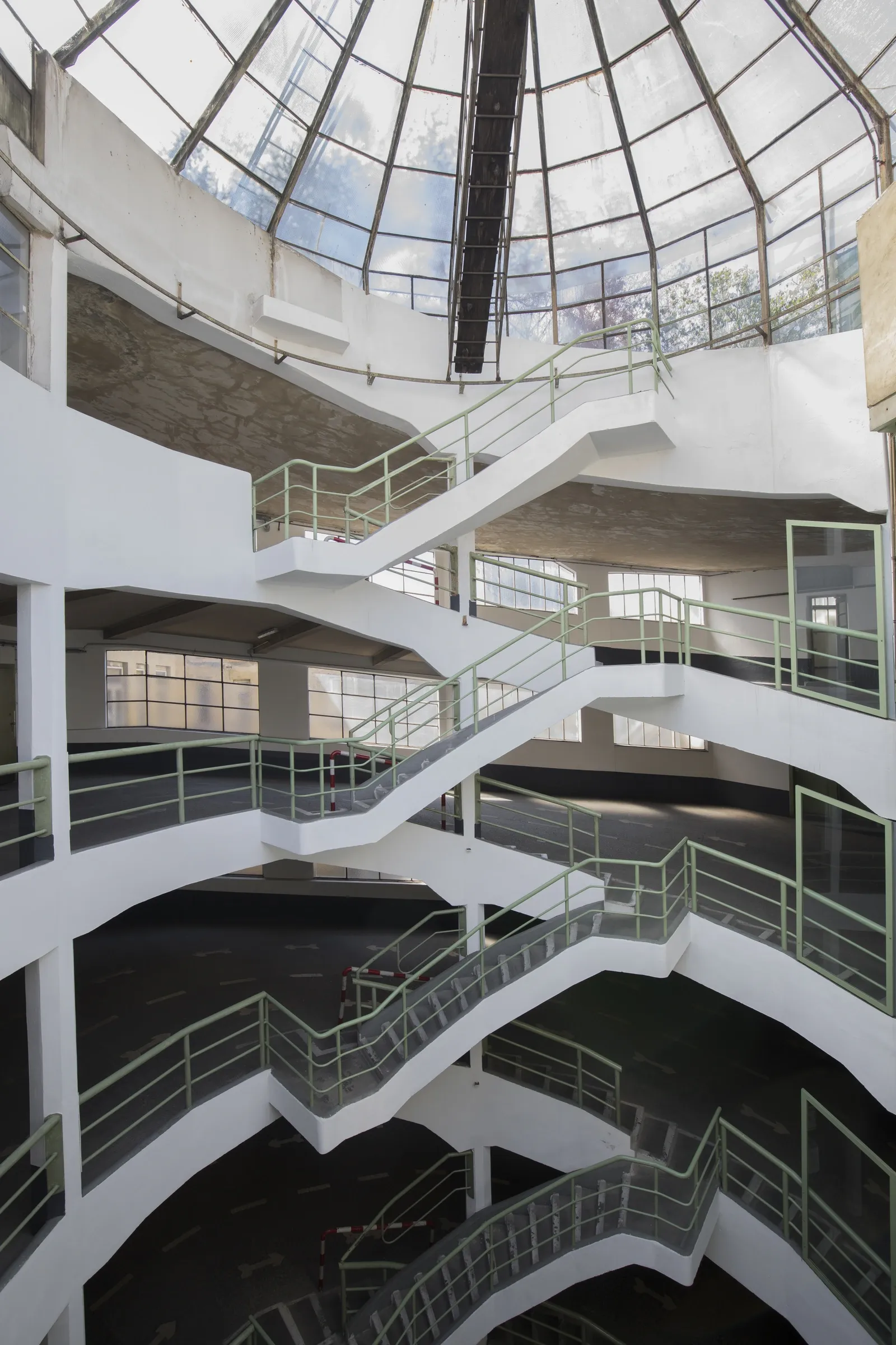 Astoria Artshow 2026: multi-level white spiral staircase with sage-green railings rising beneath the glass dome of Astoria Garage, Vienna.