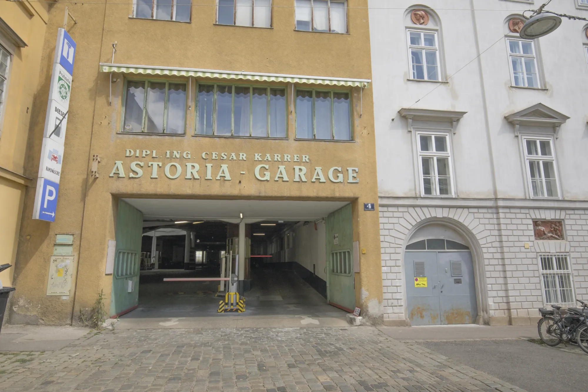 Astoria Artshow 2026: exterior of Astoria Garage in Vienna, ochre and white facade with the historic Astoria-Garage sign above the tunnel entrance ramp.