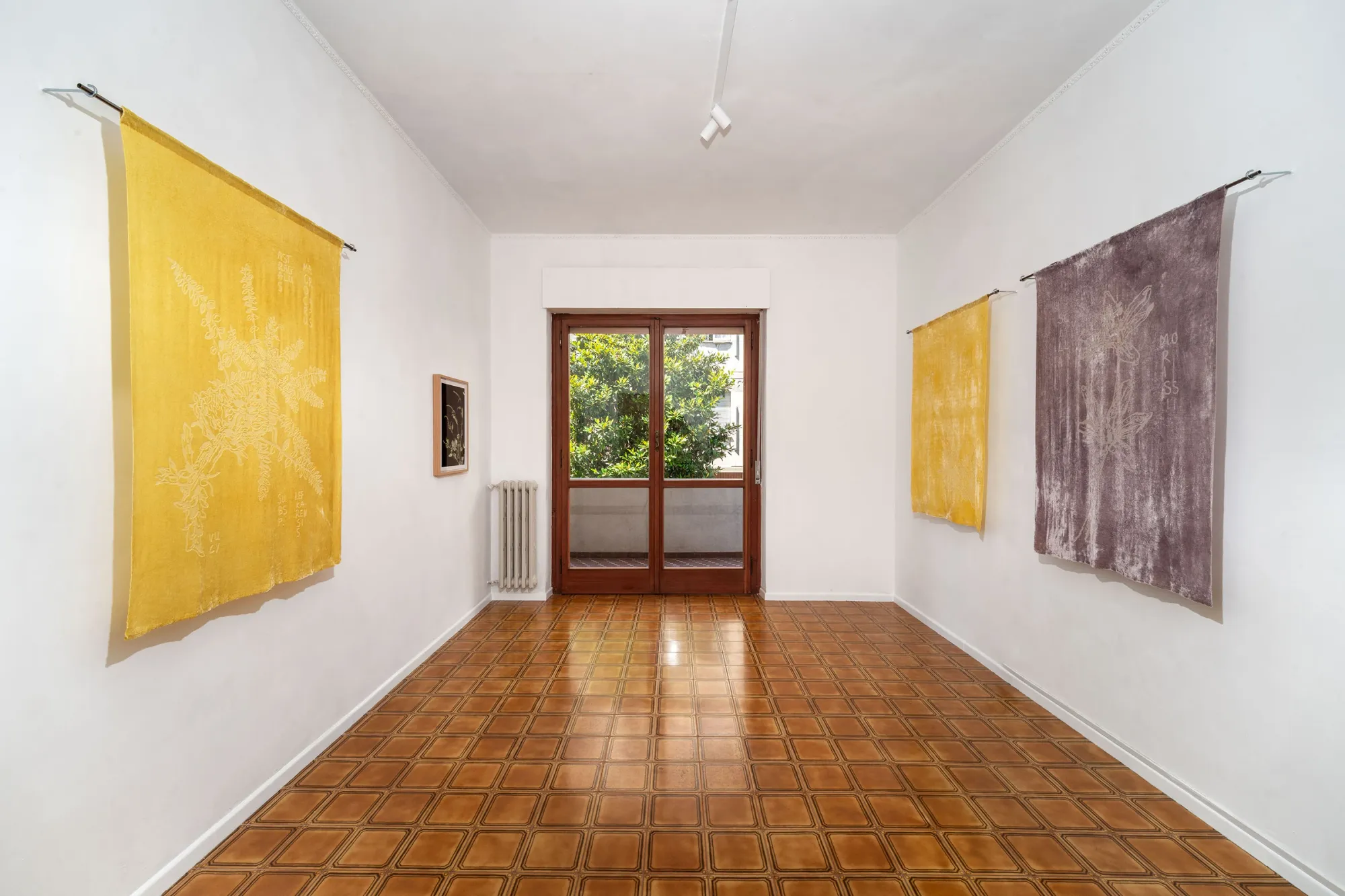 Exhibition review of Elena Adamou: Iconographies at primopiano, Montesilvano, 2026. Room hung with four botanical devoré velvet textiles in yellow and mauve tones.