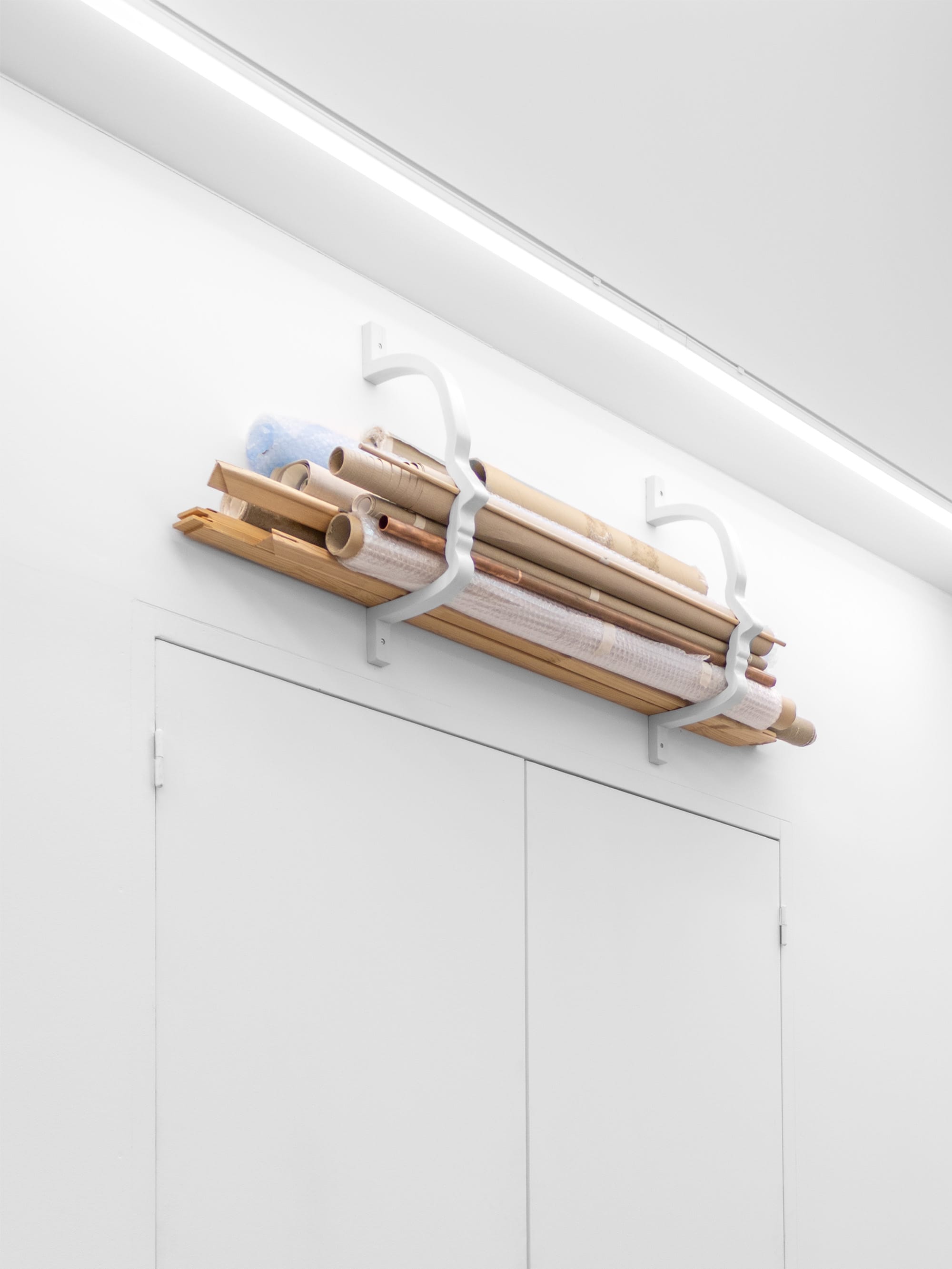 Exhibition review of Emily Dietrich: Self portrait of the artist or a storage solution for Emergency Space at Emergency Space, Paris, 2026. Wall-mounted lacquered MDF rack holding rolled paper and tubes.