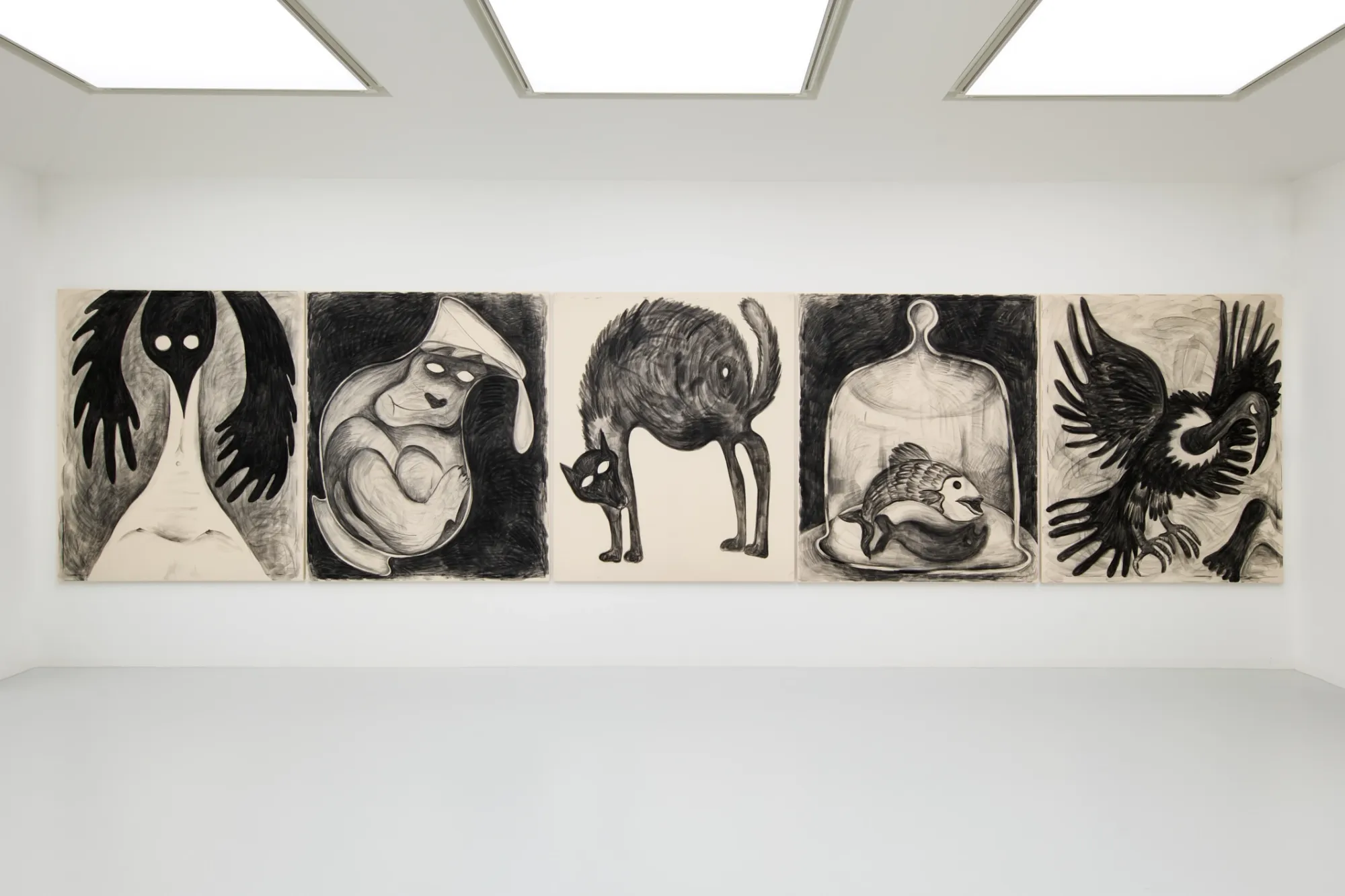 Exhibition review of Kallirroi Ioannidou: Galvanizing Memories at Kallmann-Museum, Ismaning, 2026. Row of five large charcoal drawings, a standing figure with wide wing shapes for arms, a curled form wrapped in a pointed hood, a cat bent forward with an arched spine, a fish under a glass cloche, and a raven with both wings spread open.